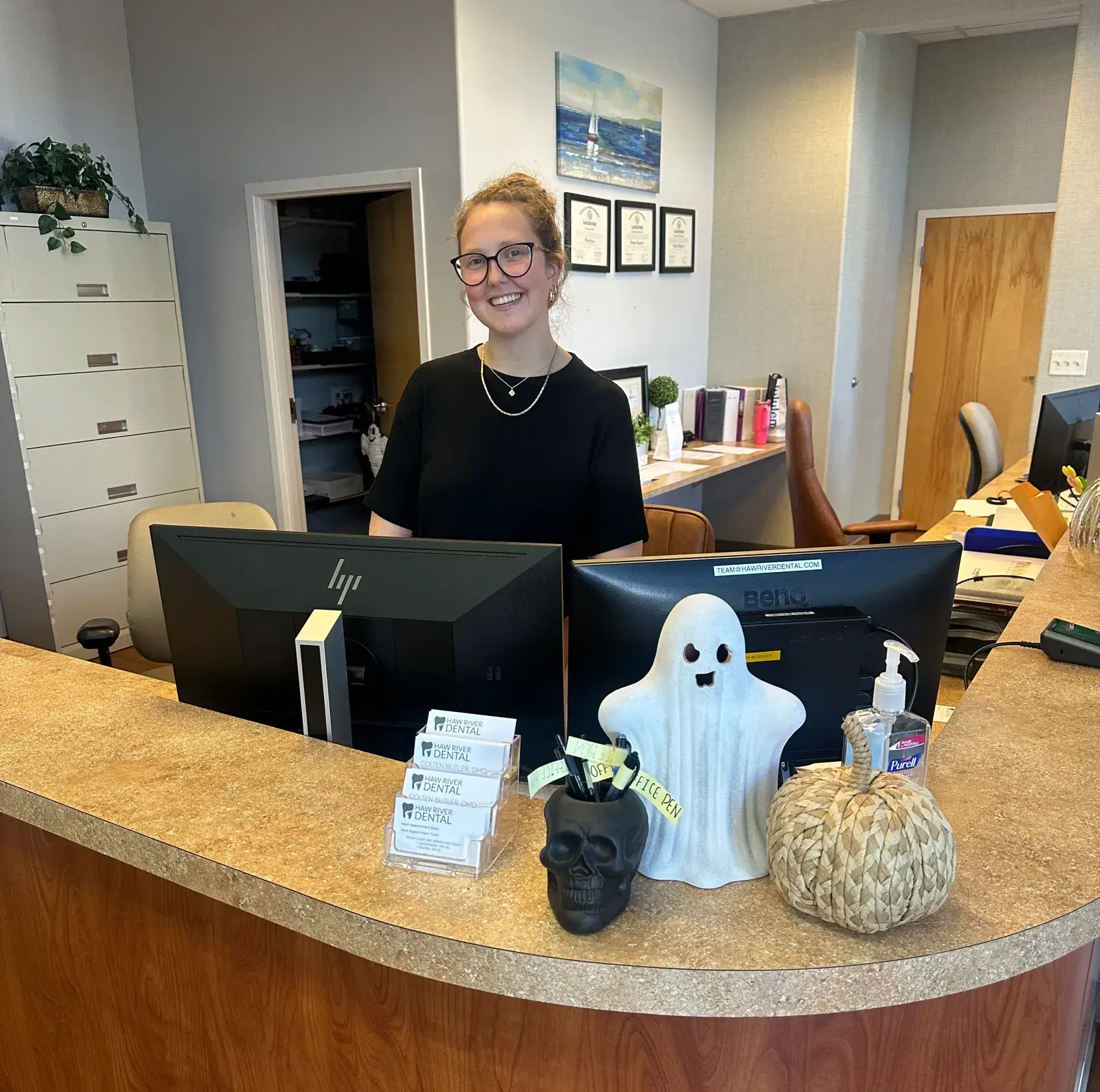 A person stands behind a reception desk decorated with Halloween items, including a ghost and skull.