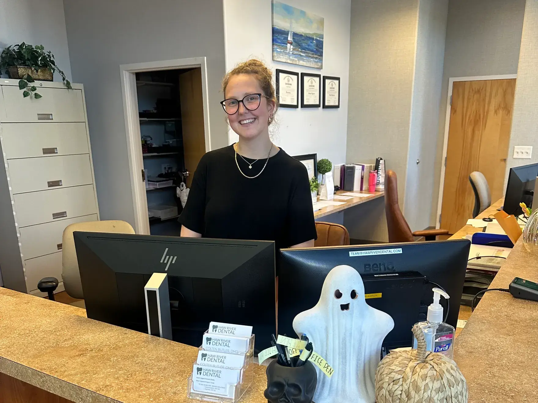 A person stands smiling behind a desk with Halloween decorations, including a ghost and skull.