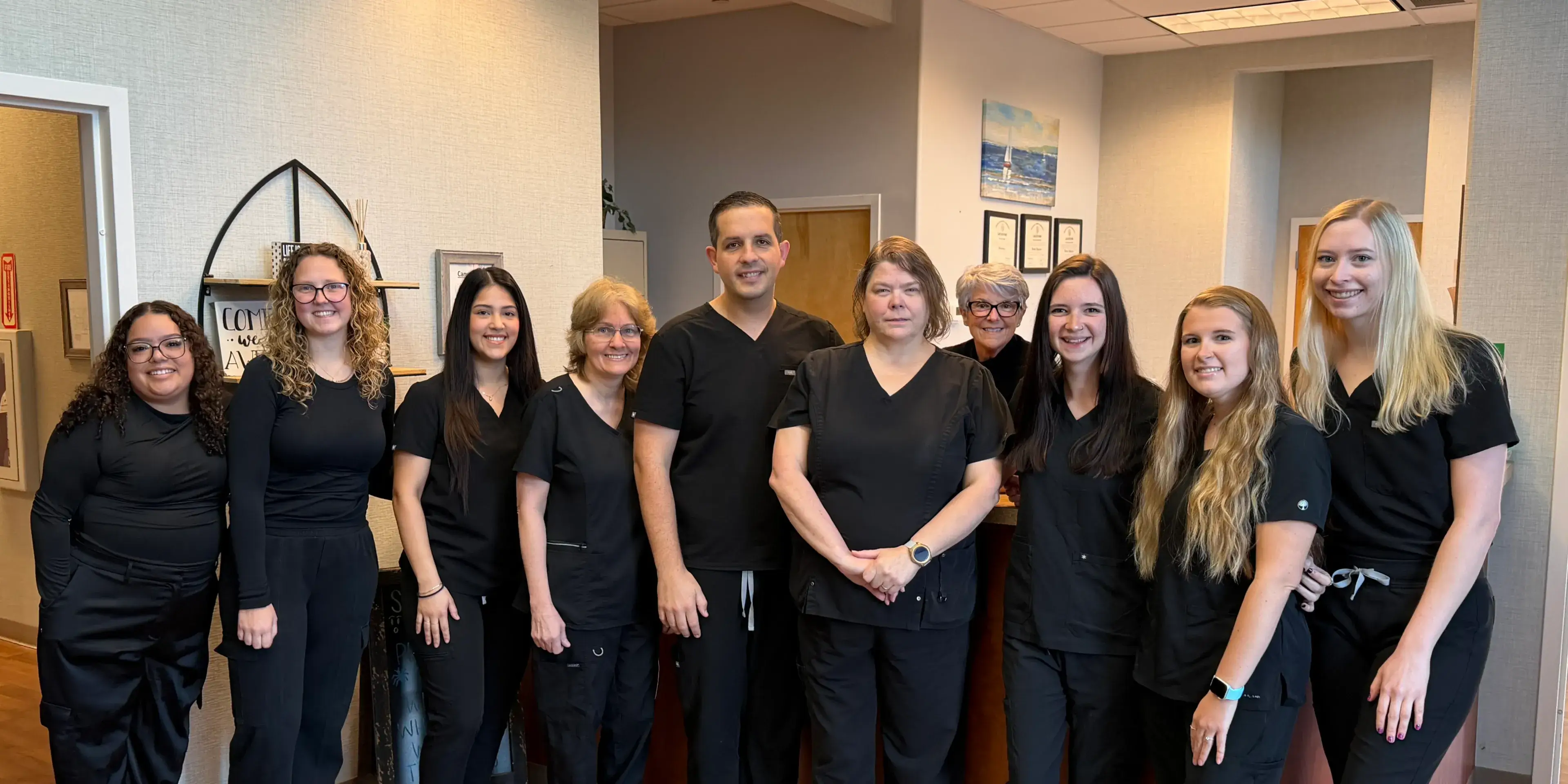 A group of ten people in black uniforms stands together, smiling in an office setting.