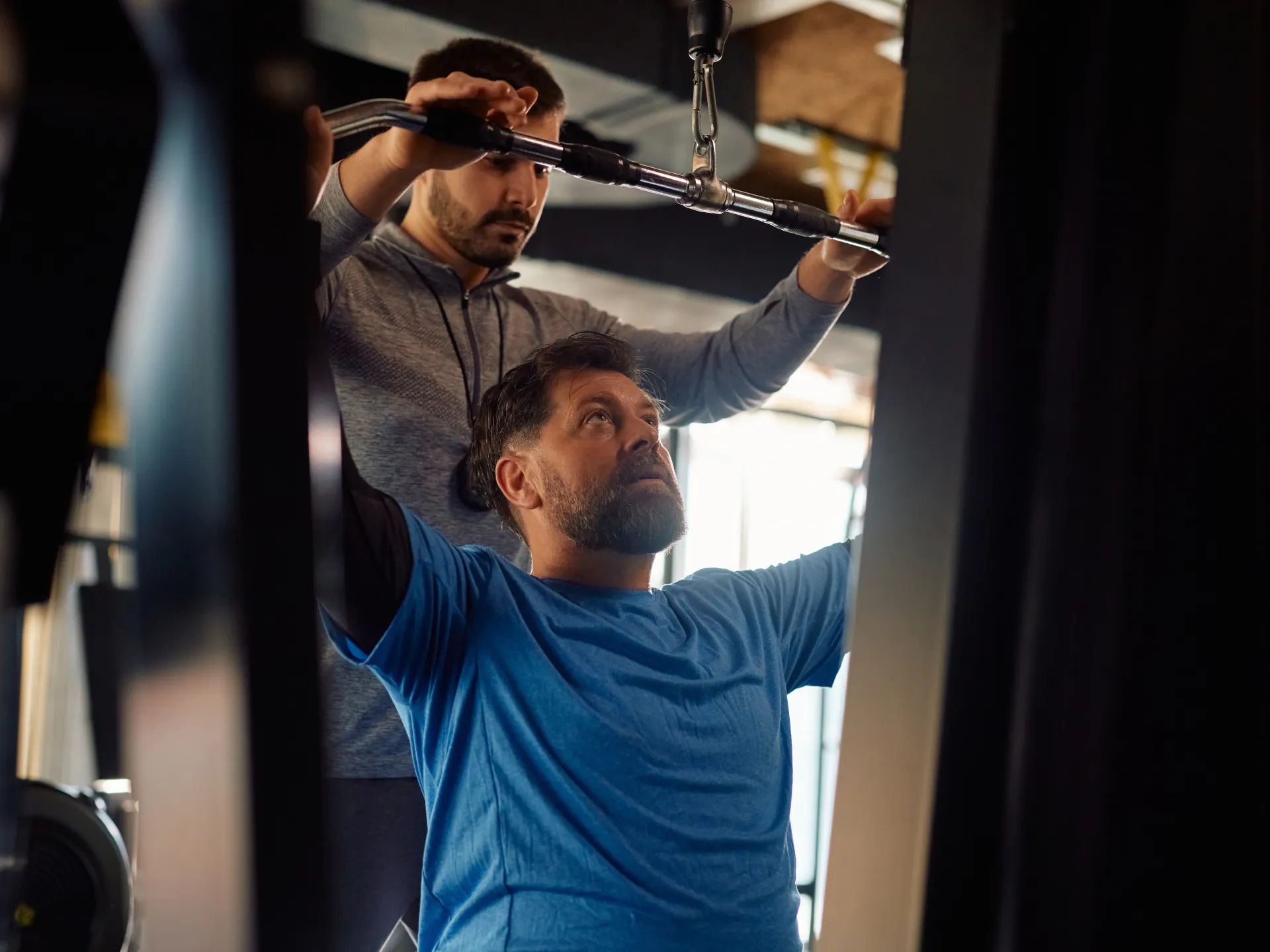 Entraineur privé guidant un sportif à la poulie en salle de musculation