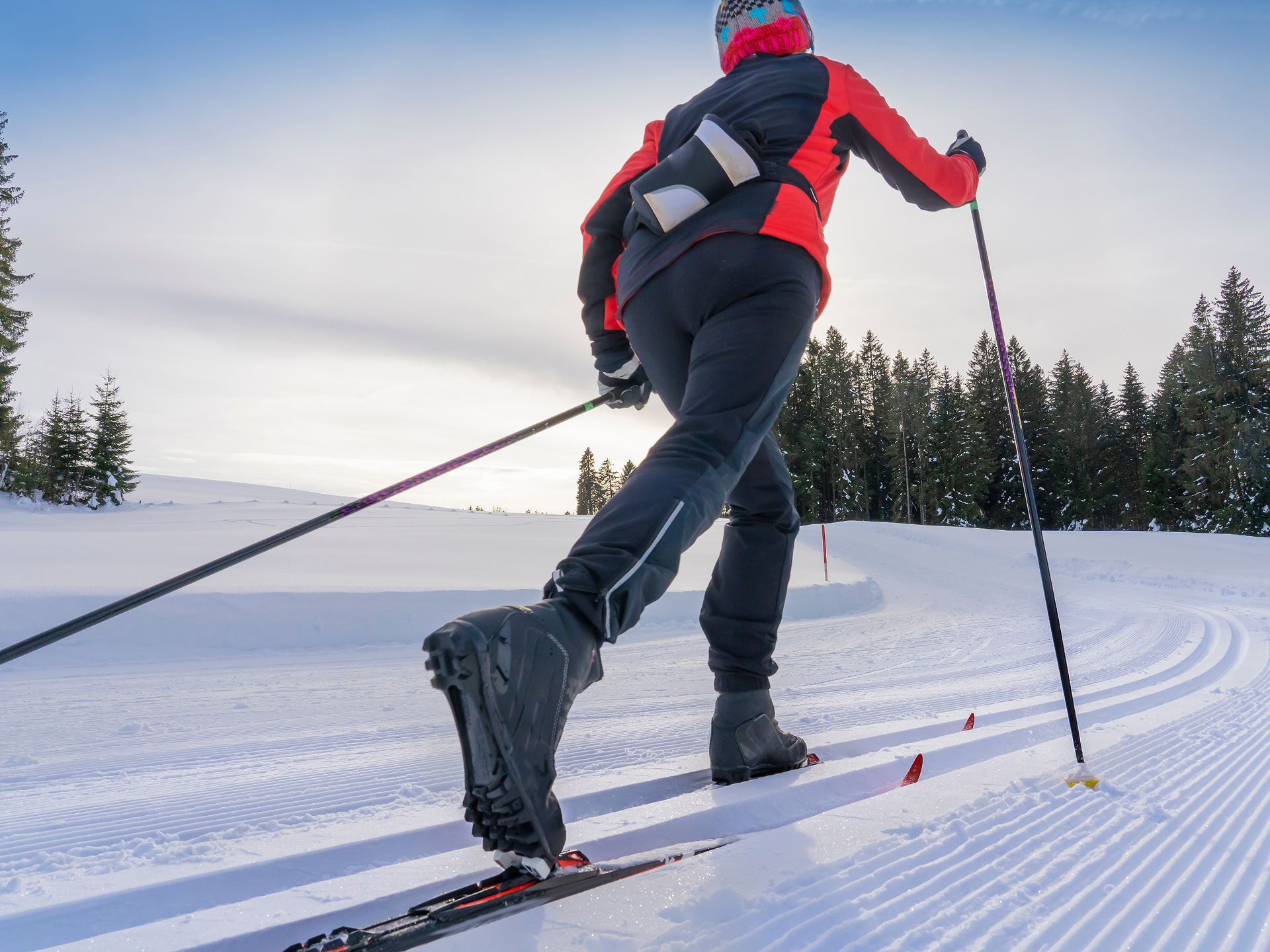 Skieuse de fond sur une piste damée, entre les sapins enneigés