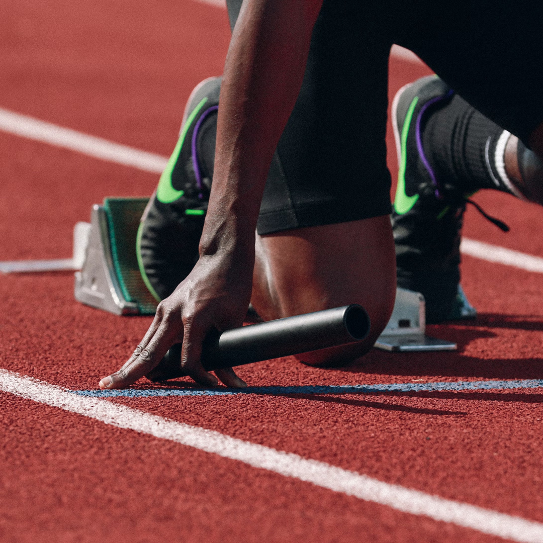 Sprinteur dans les starting-blocks, témoin de relais en main, sur une piste d'athlétisme
