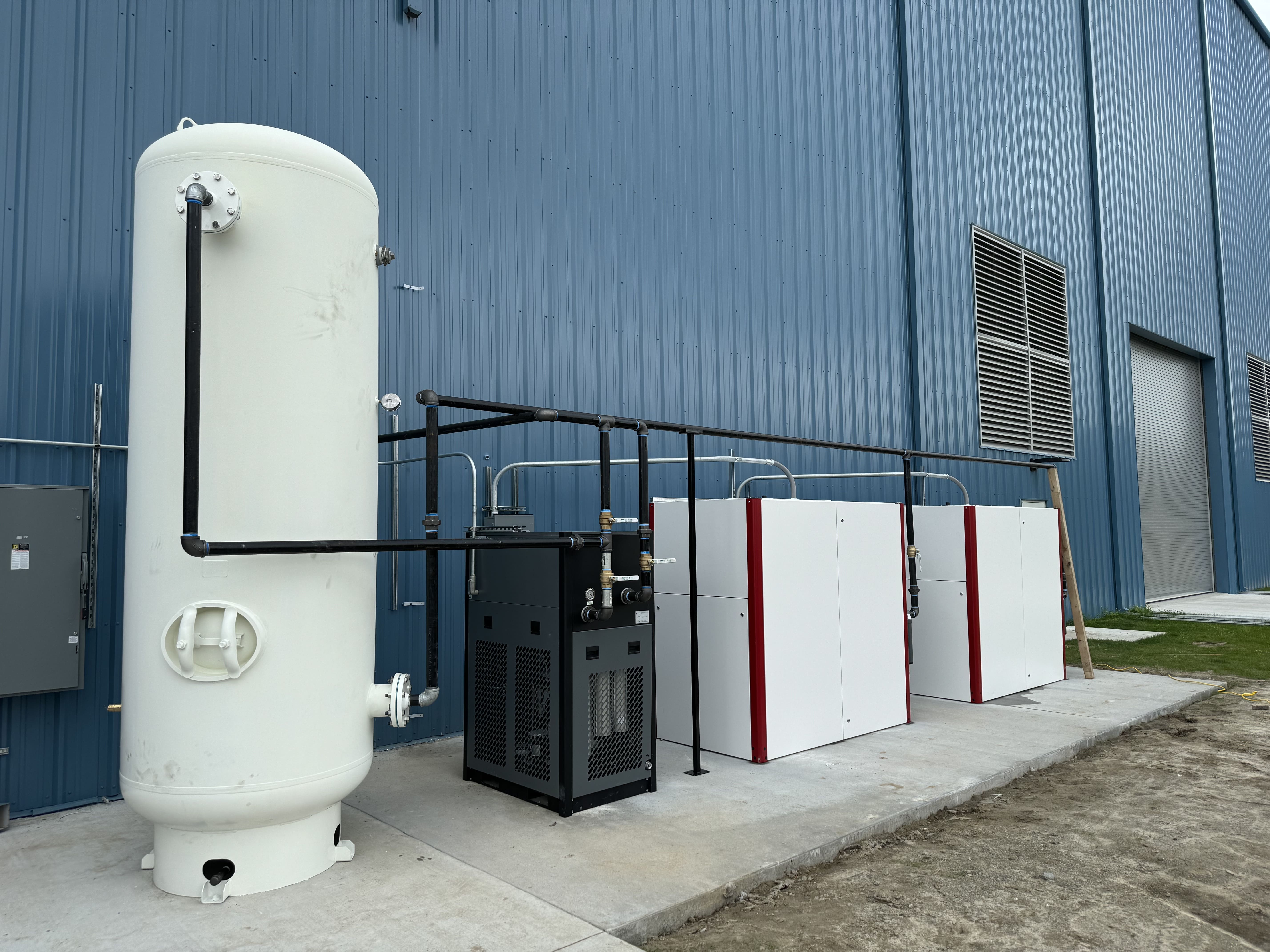Two industrial air compressors connected to a full air system installed outside a commercial facility