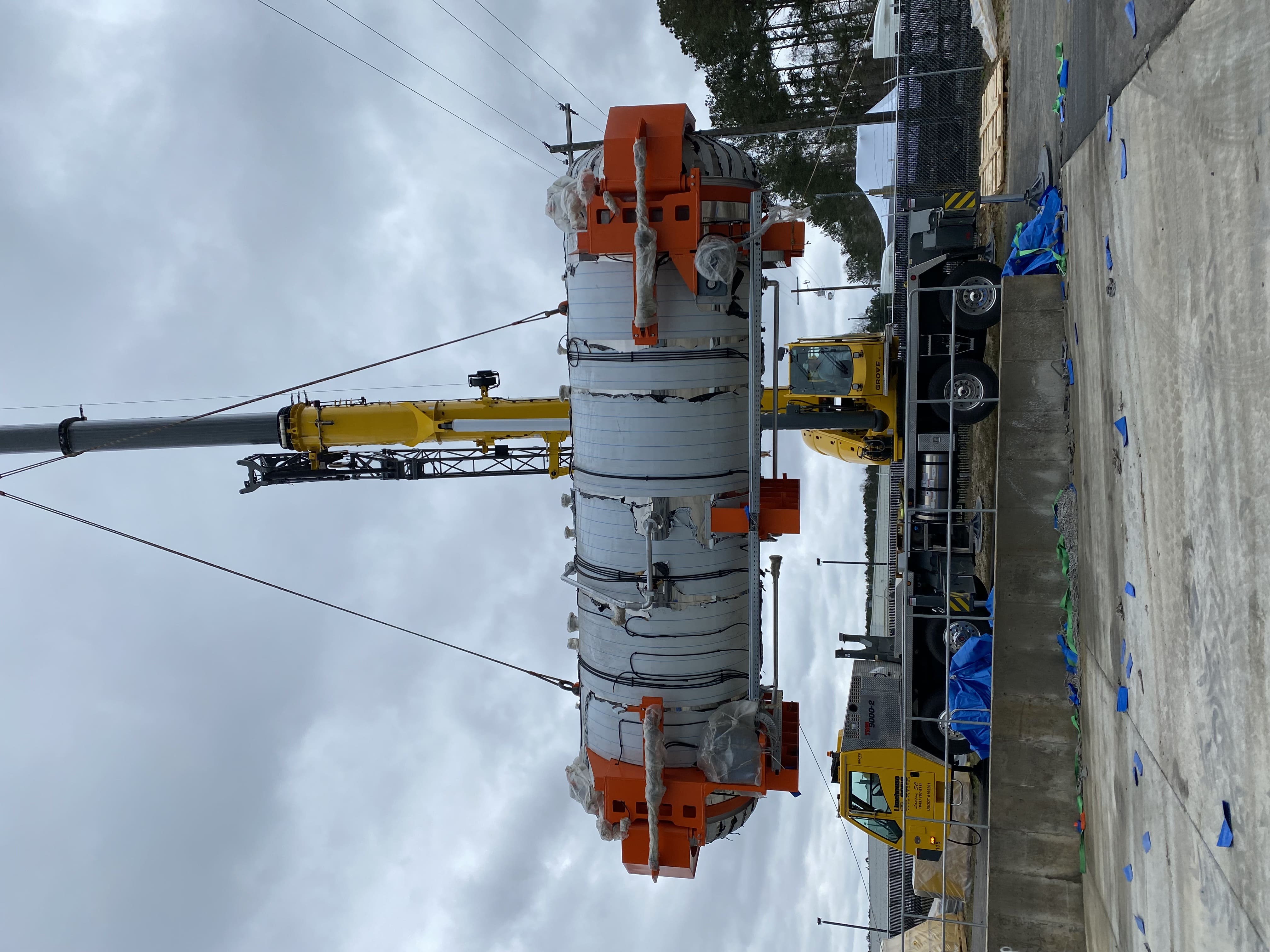 yellow crane rig lifting large mechanical system near a truck loading bay