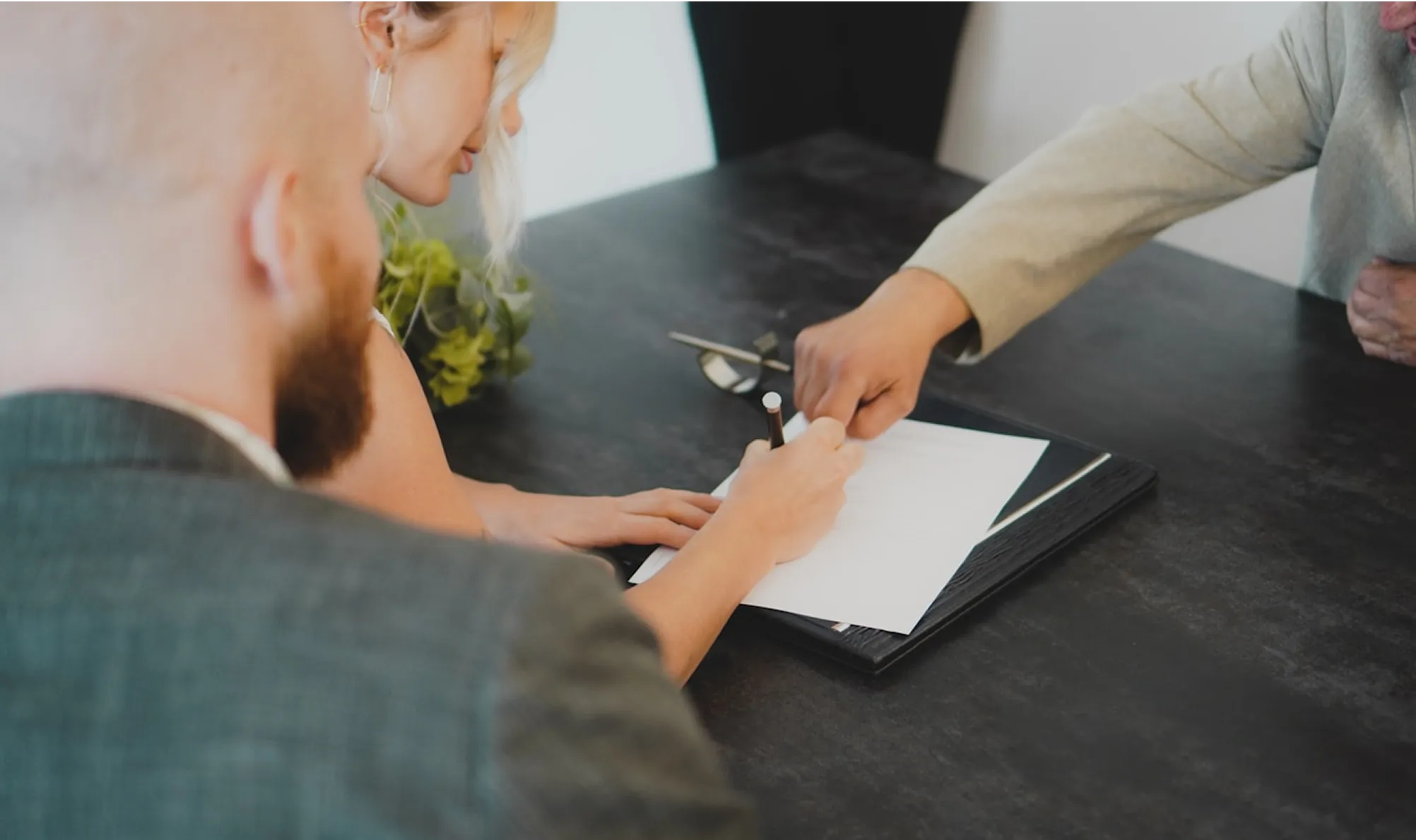 Two people signing document at a black table with plant nearby