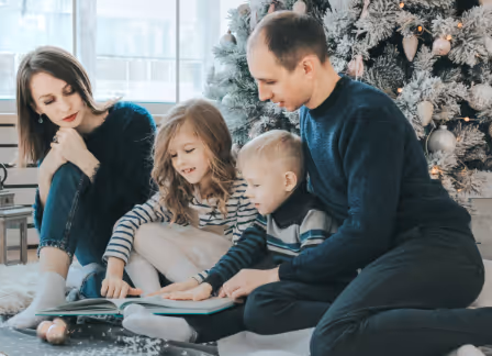 Family reading book together near Christmas tree, cozy winter scene