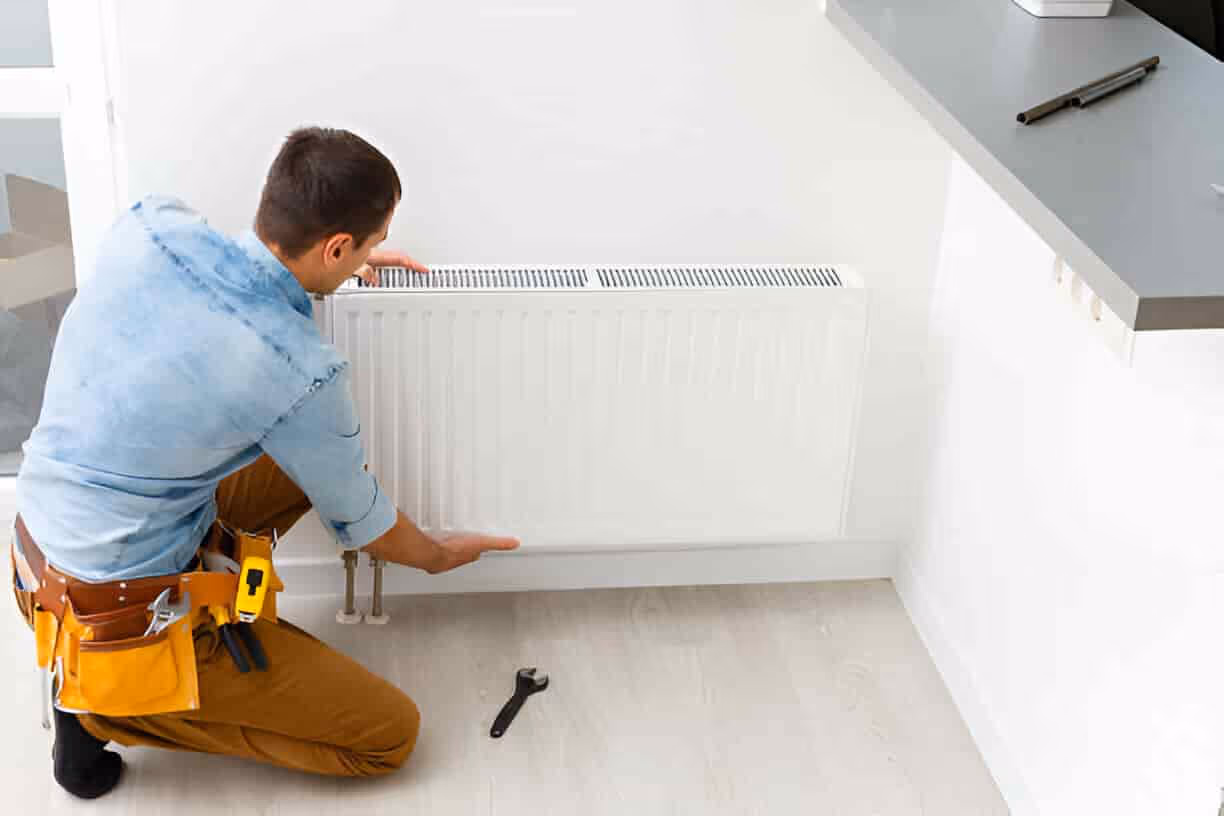Technician in work gear checking a white wall-mounted radiator