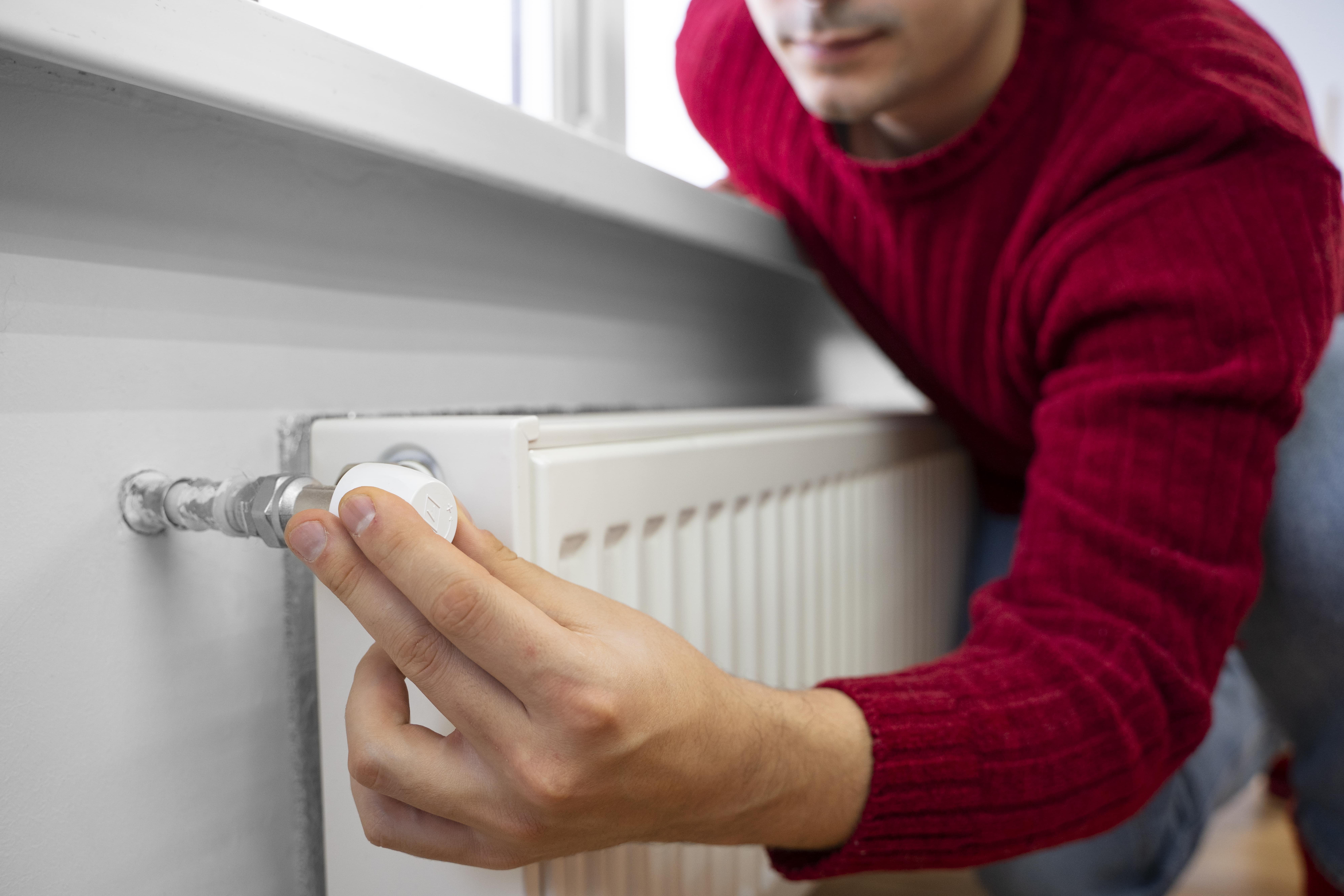 Person in red sweater adjusting thermostat on home radiator heater