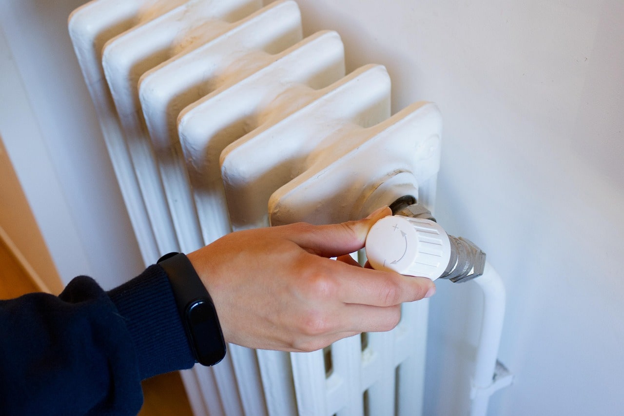 Hand adjusting white radiator valve for home heating temperature
