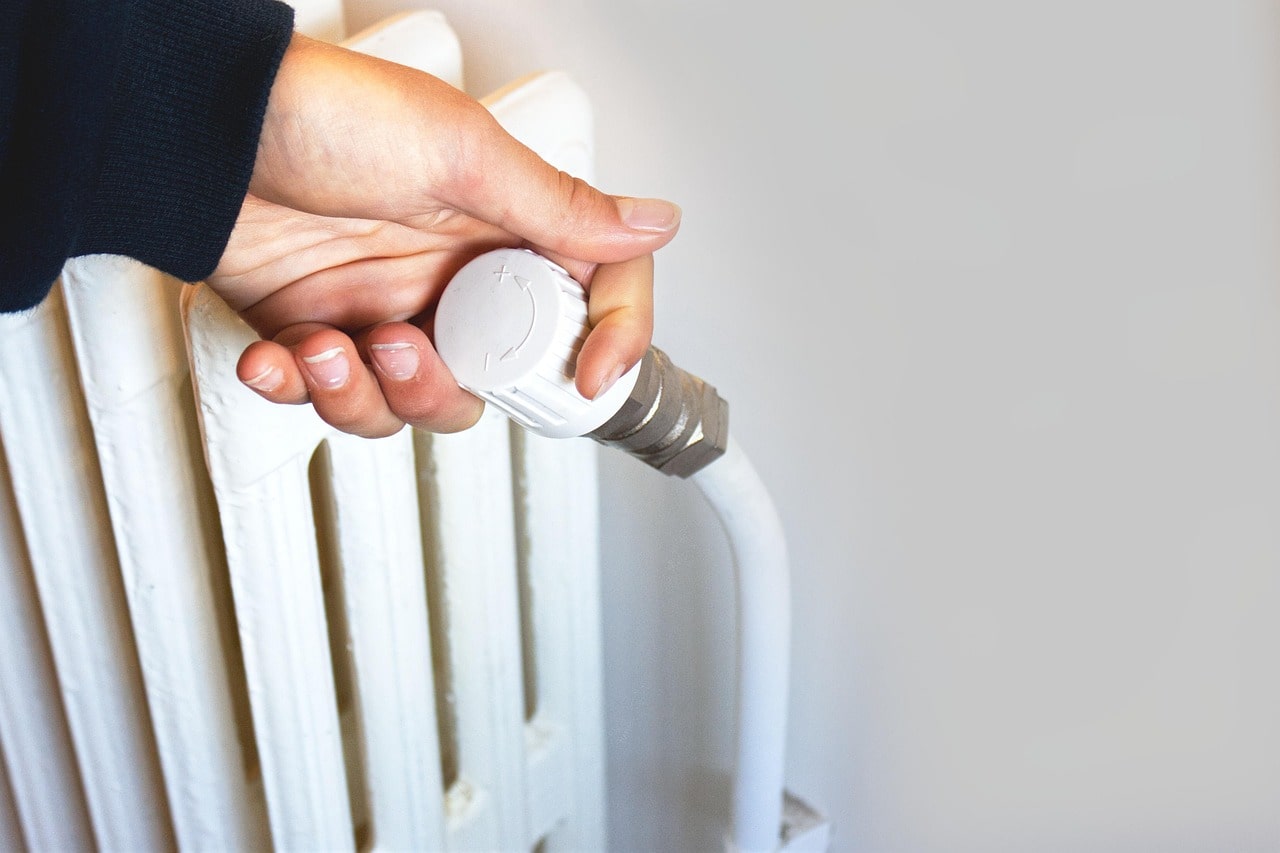 Hand adjusting white radiator thermostat valve for temperature control