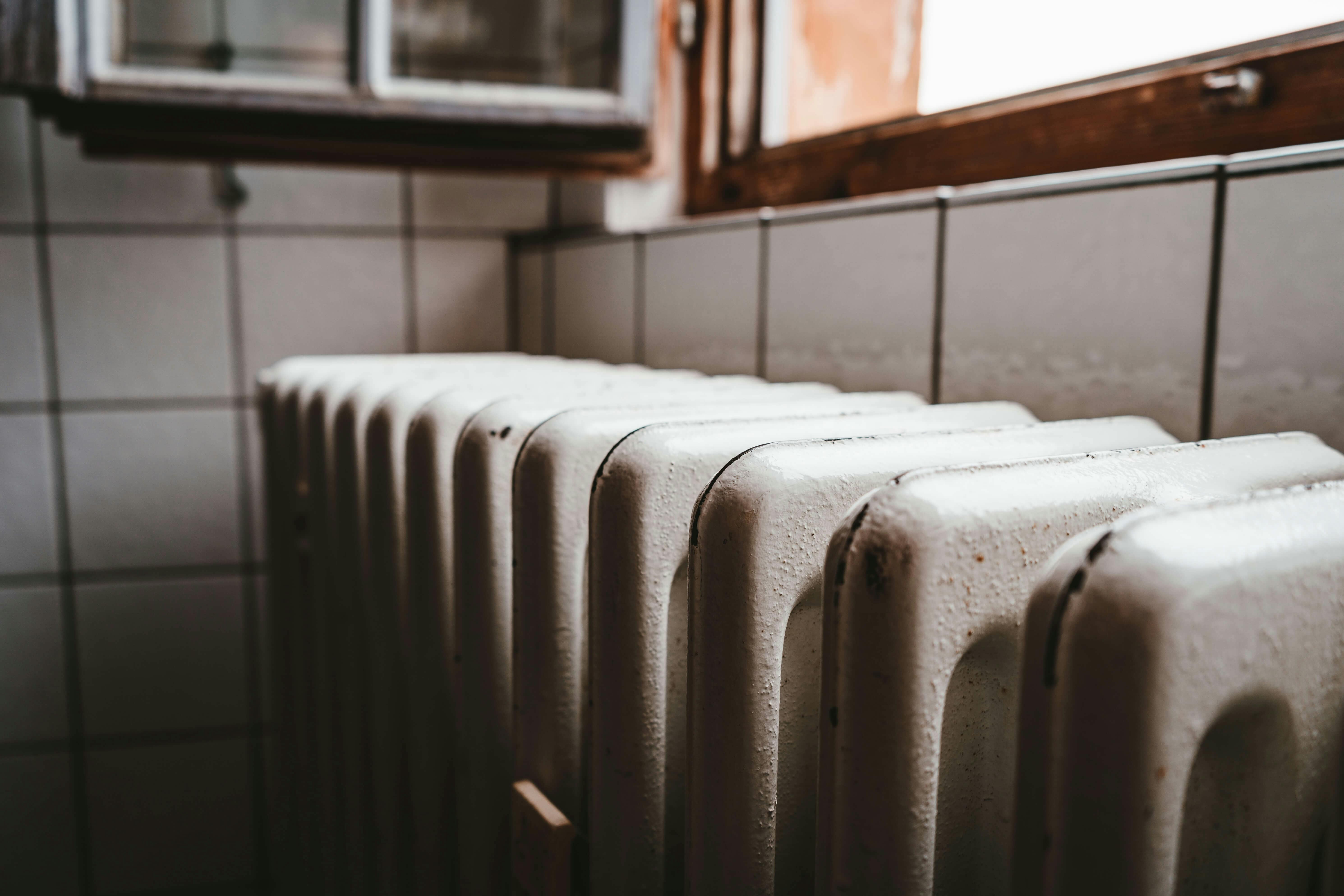 Old white radiator with ribbed design against tiled bathroom wall