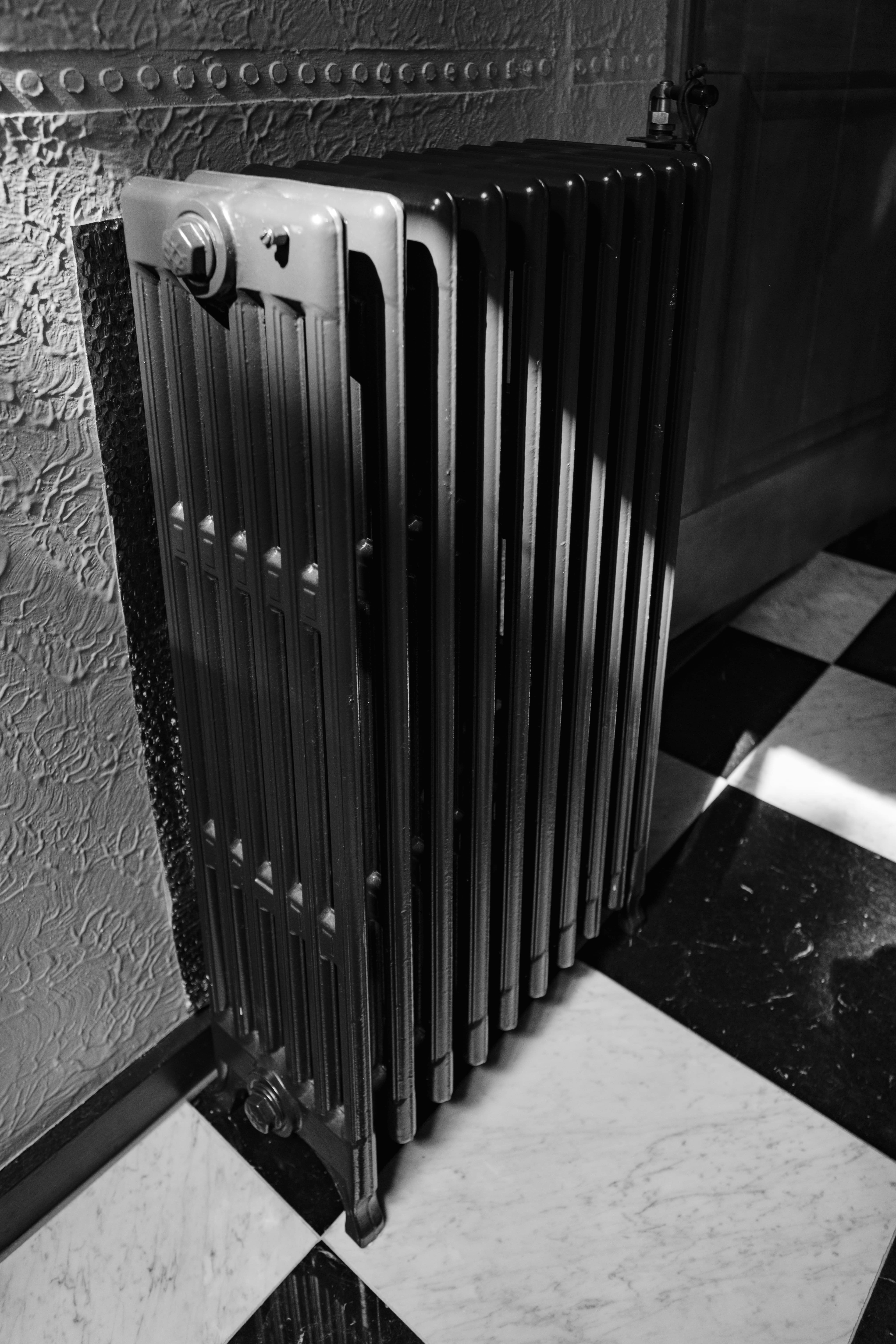 Vintage radiator mounted on textured wall with black and white checkered floor