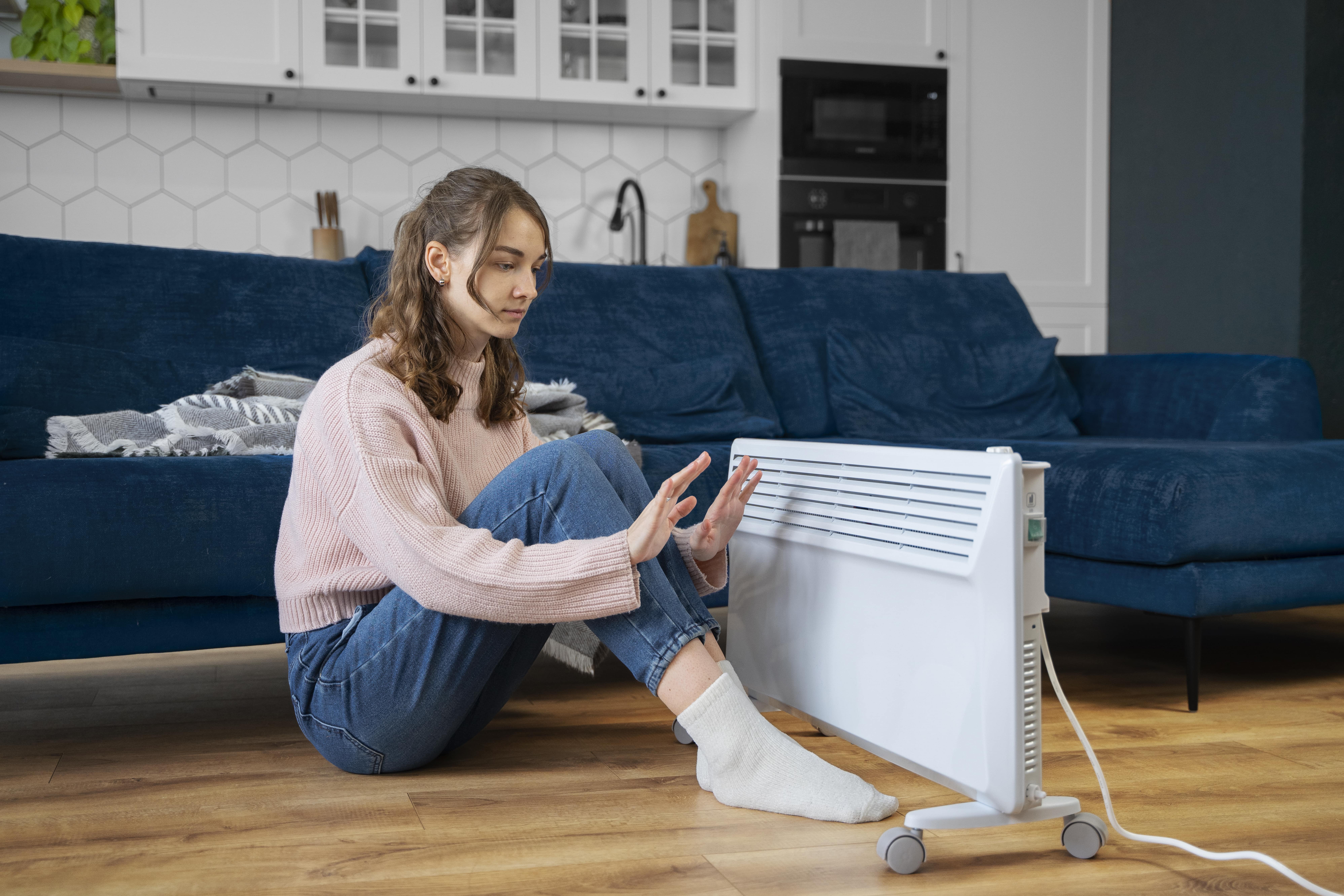 Person warming hands on electric heater in cozy living room