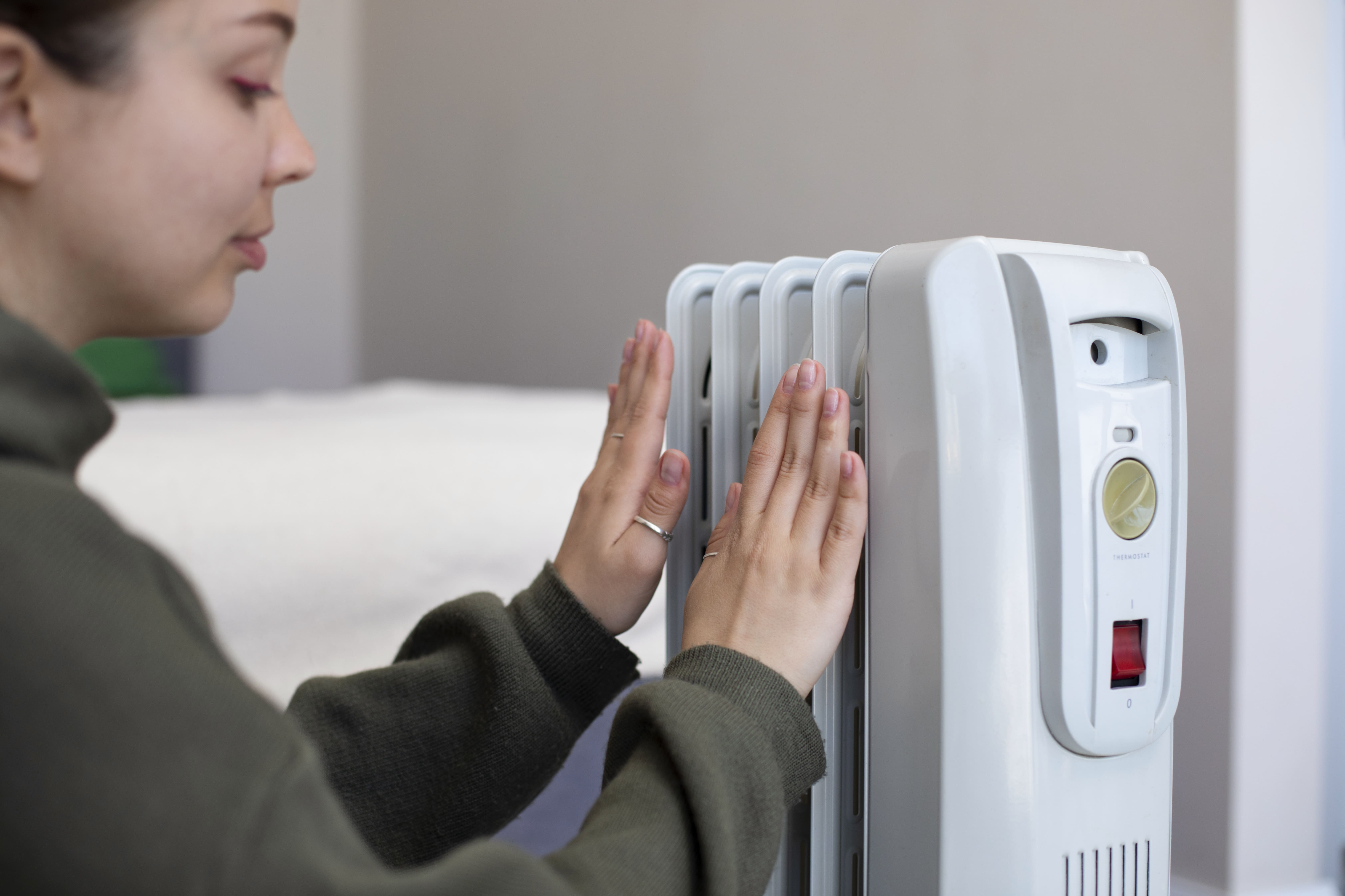 Person warming hands on white electric oil-filled radiator heater