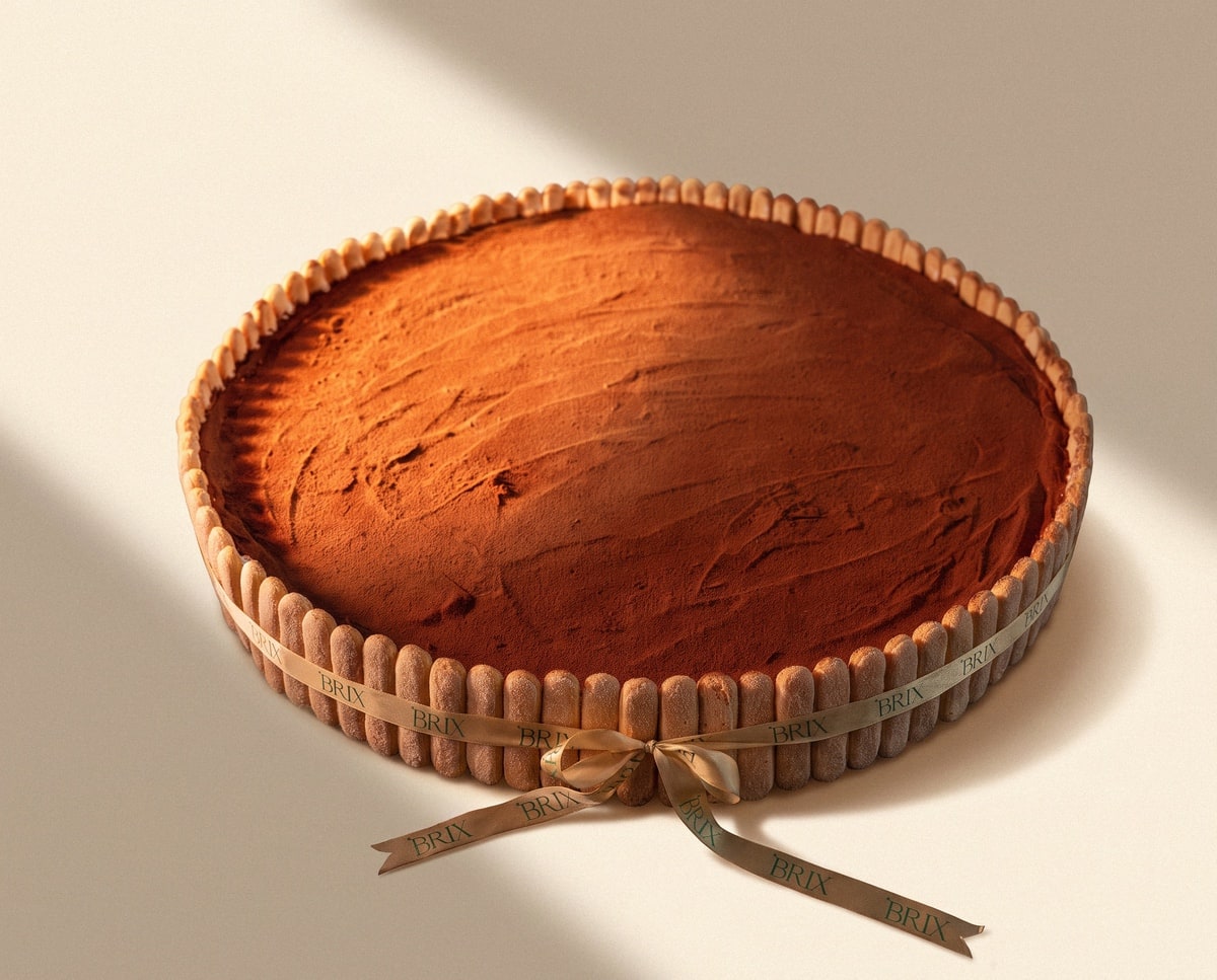 Large round tiramisu tart edged with ladyfingers, finished with swirled cocoa and a BRIX ribbon bow