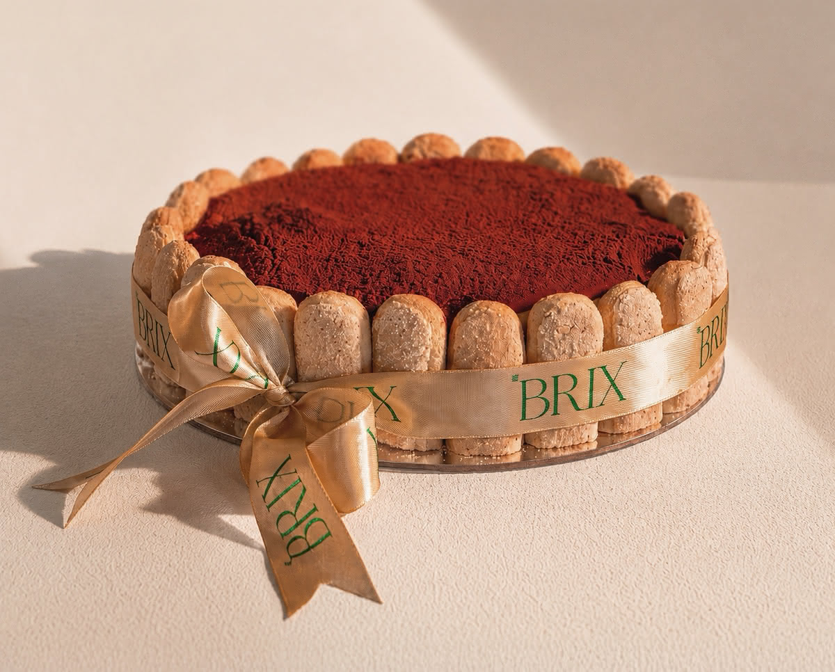 Round tiramisu cake bordered with ladyfinger biscuits, dusted with cocoa and tied with a gold BRIX ribbon