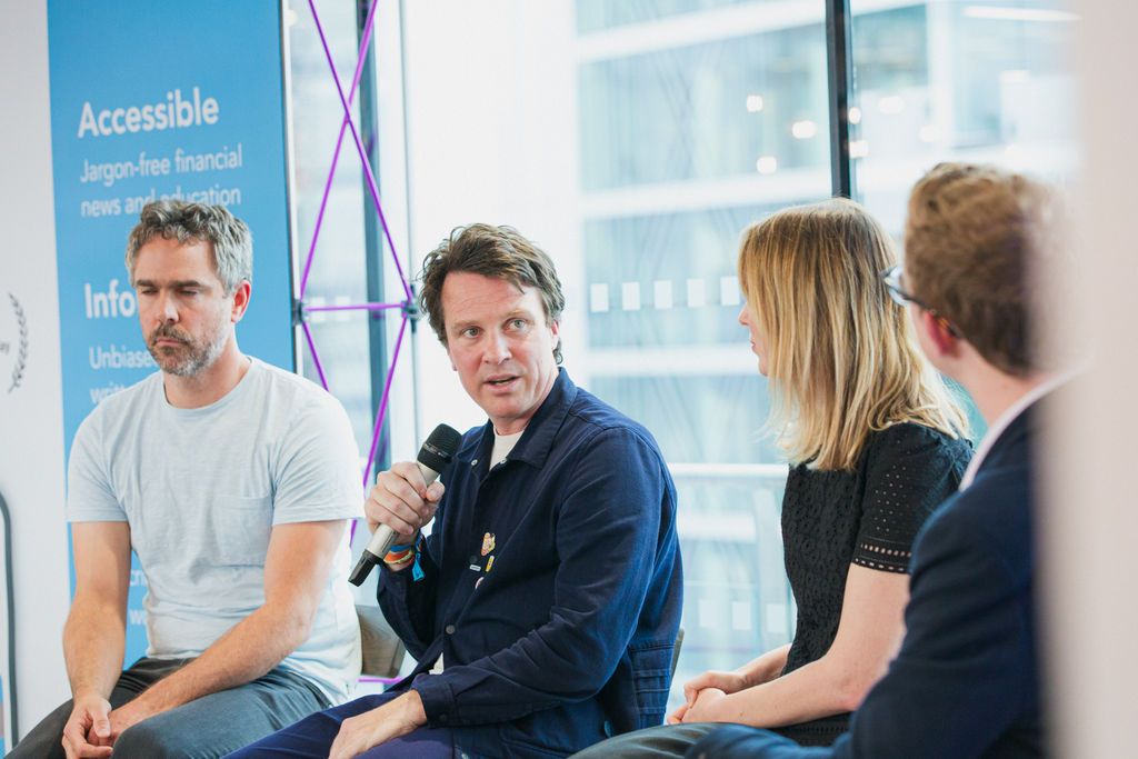 Two mean and a woman listen as another man speaks into a microphone.
