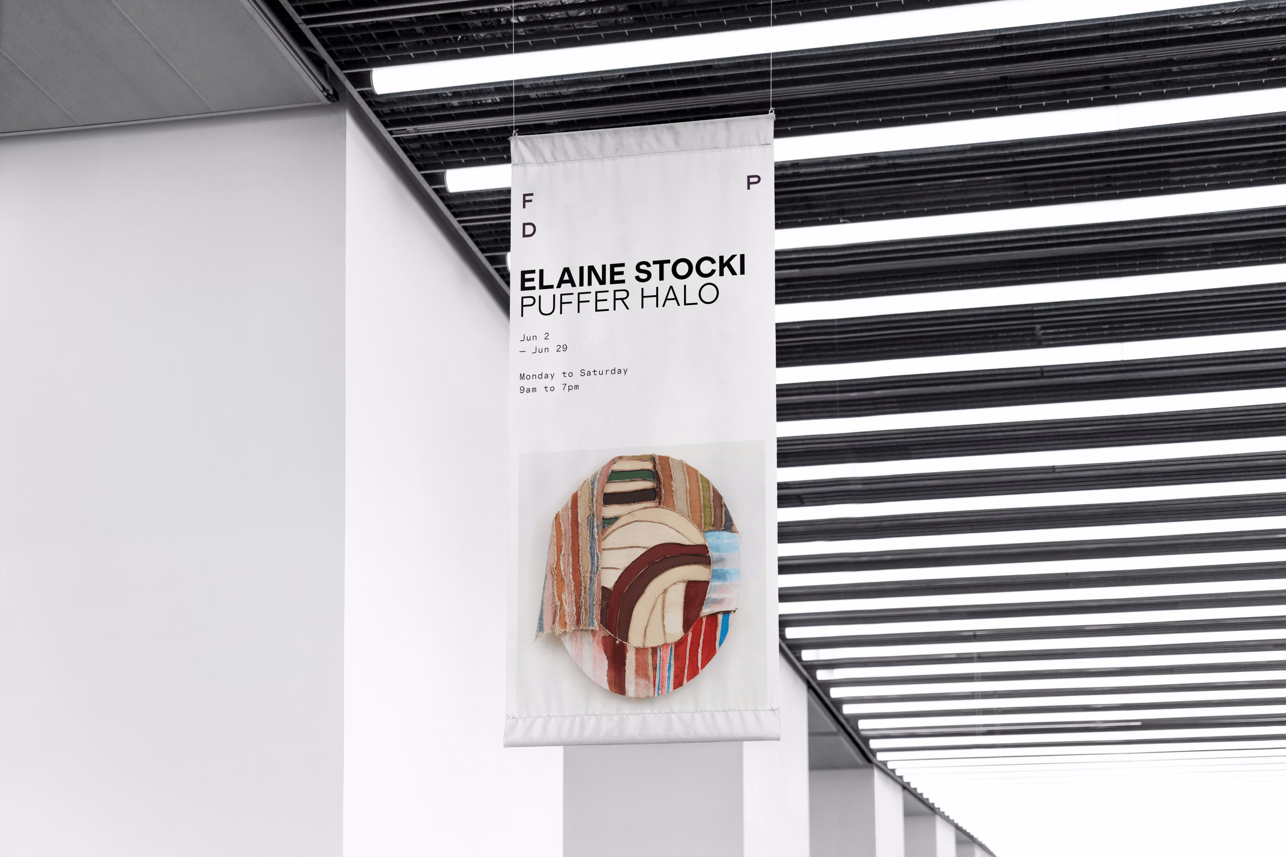 White hanging banner in a modern gallery featuring text 'Elaine Stocki Puffer Halo' with exhibition dates and image of circular abstract textile art.