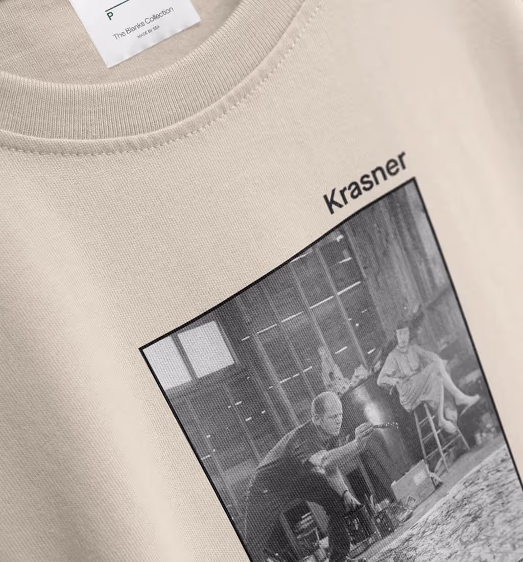 Close-up of beige t-shirt with a black and white photo of artists working, labeled 'Krasner' above the image.