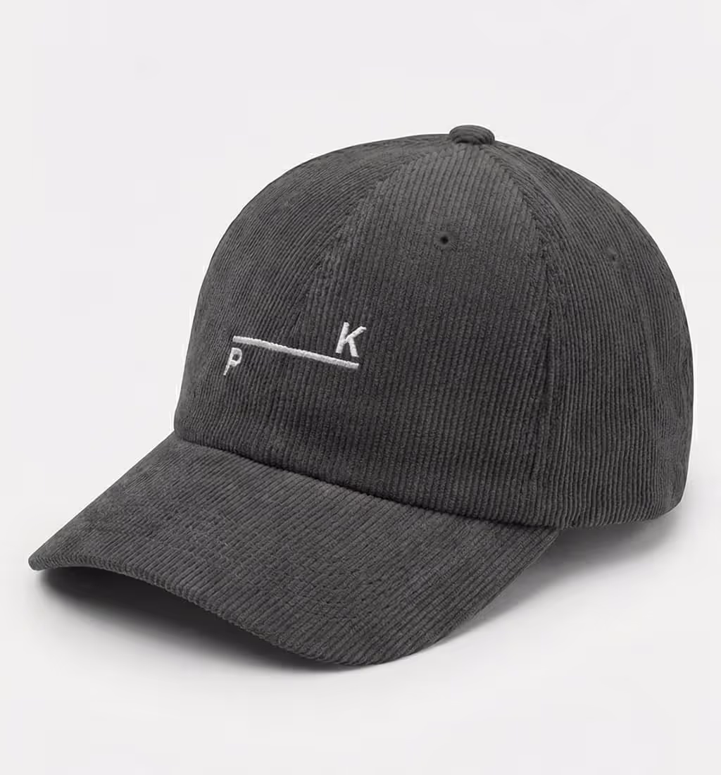 Black corduroy baseball cap with white minimalist embroidery of letters 'P' and 'K' separated by a horizontal line.