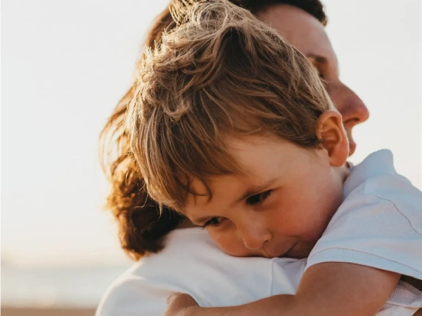 Young boy hugging an adult tightly on a beach at sunset.