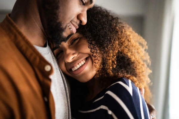 A smiling woman with curly hair hugging a man with a beard and lip piercing.