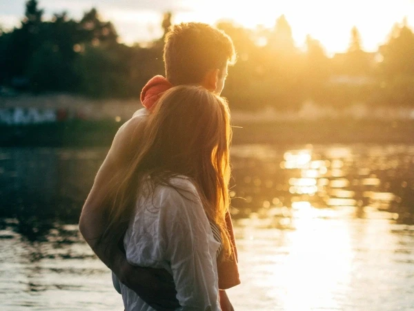 Couple embracing by a lake at sunset with sunlight reflecting on the water.