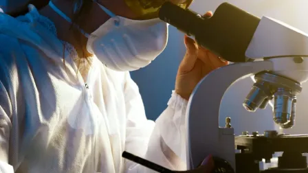 Scientist looking into a microscope to evaluate genetic test sample 