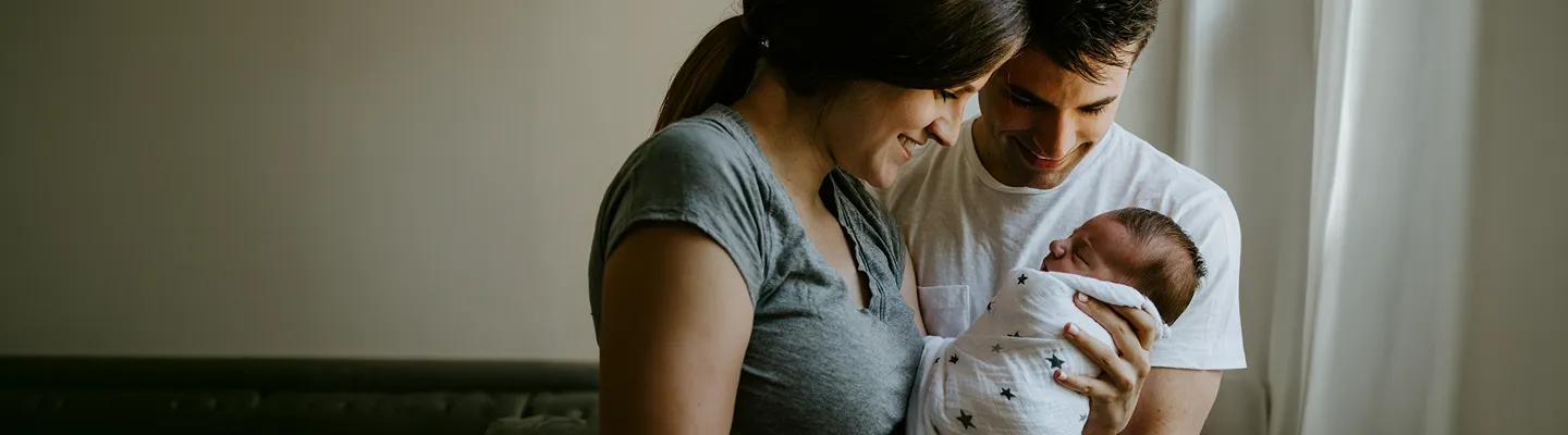 Smiling parents holding their newborn baby wrapped in a star-patterned blanket indoors.