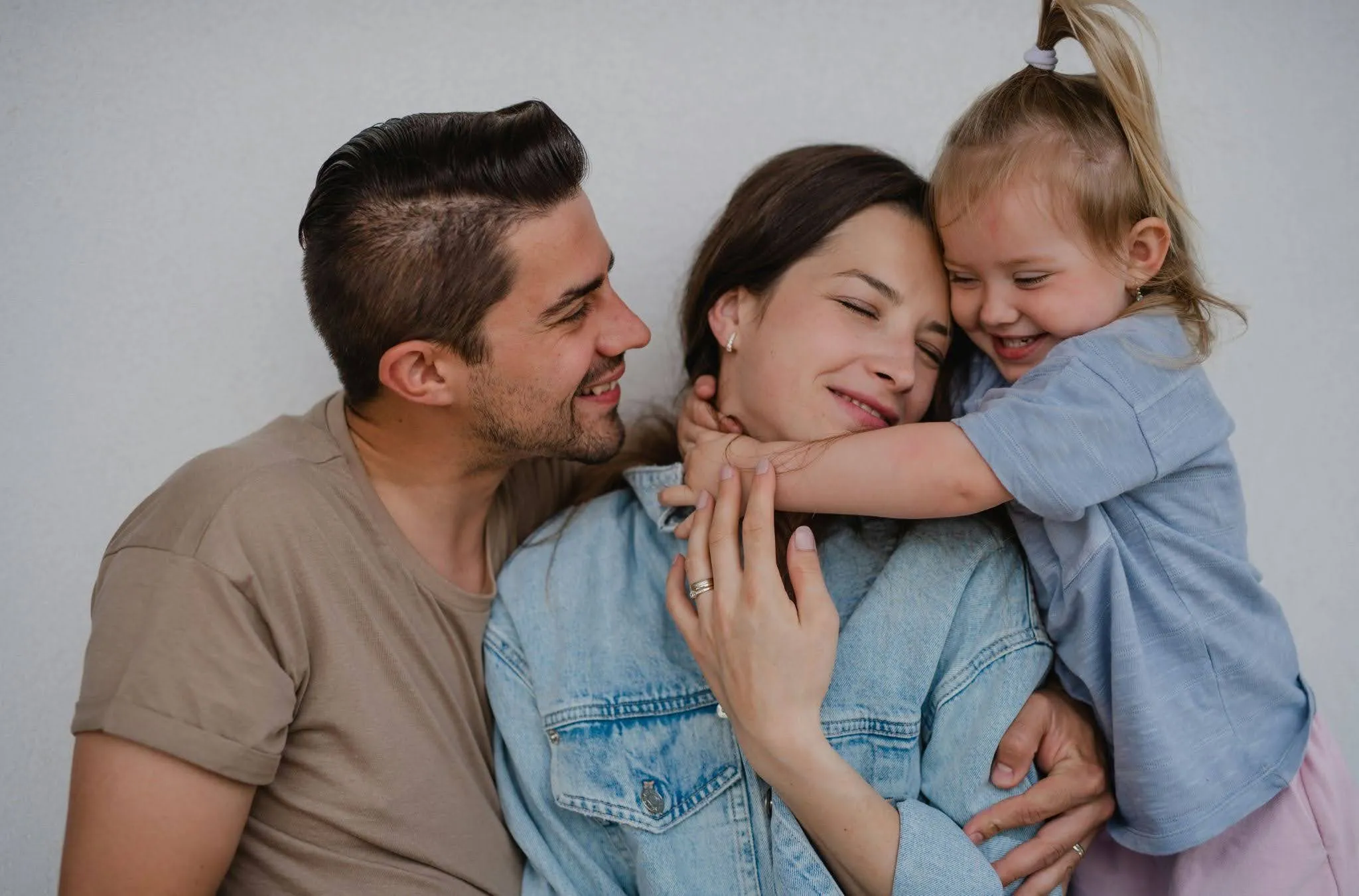 Smiling parents embrace their young daughter who hugs her mother affectionately.