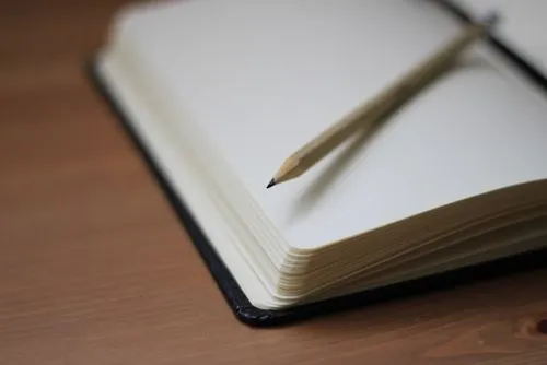 corner of an open blank journal with a pencil on top