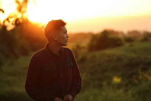 man standing in a field at sunset looking pensive