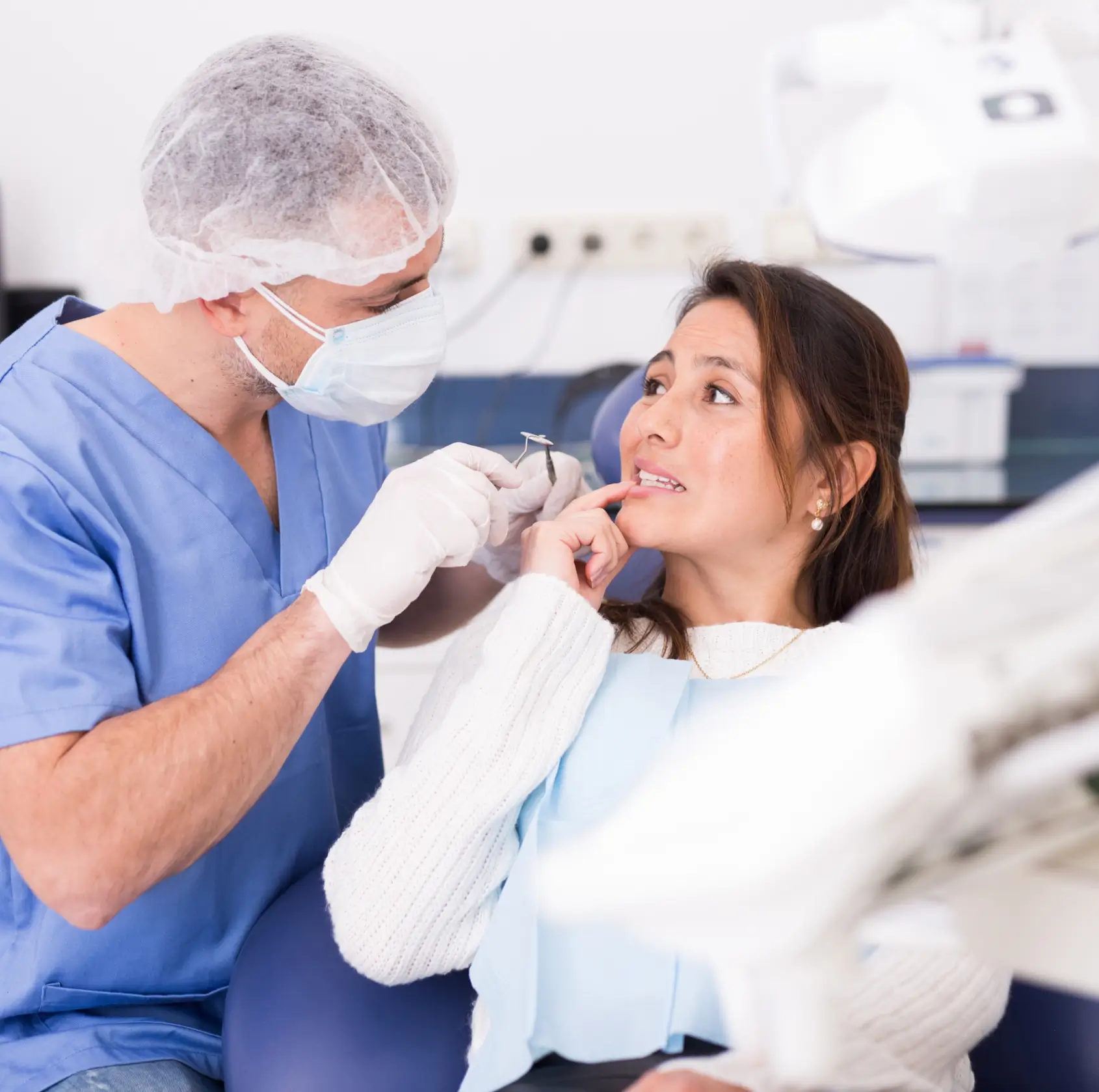Dentist examines a woman's teeth while she points to her mouth in a dental office.
