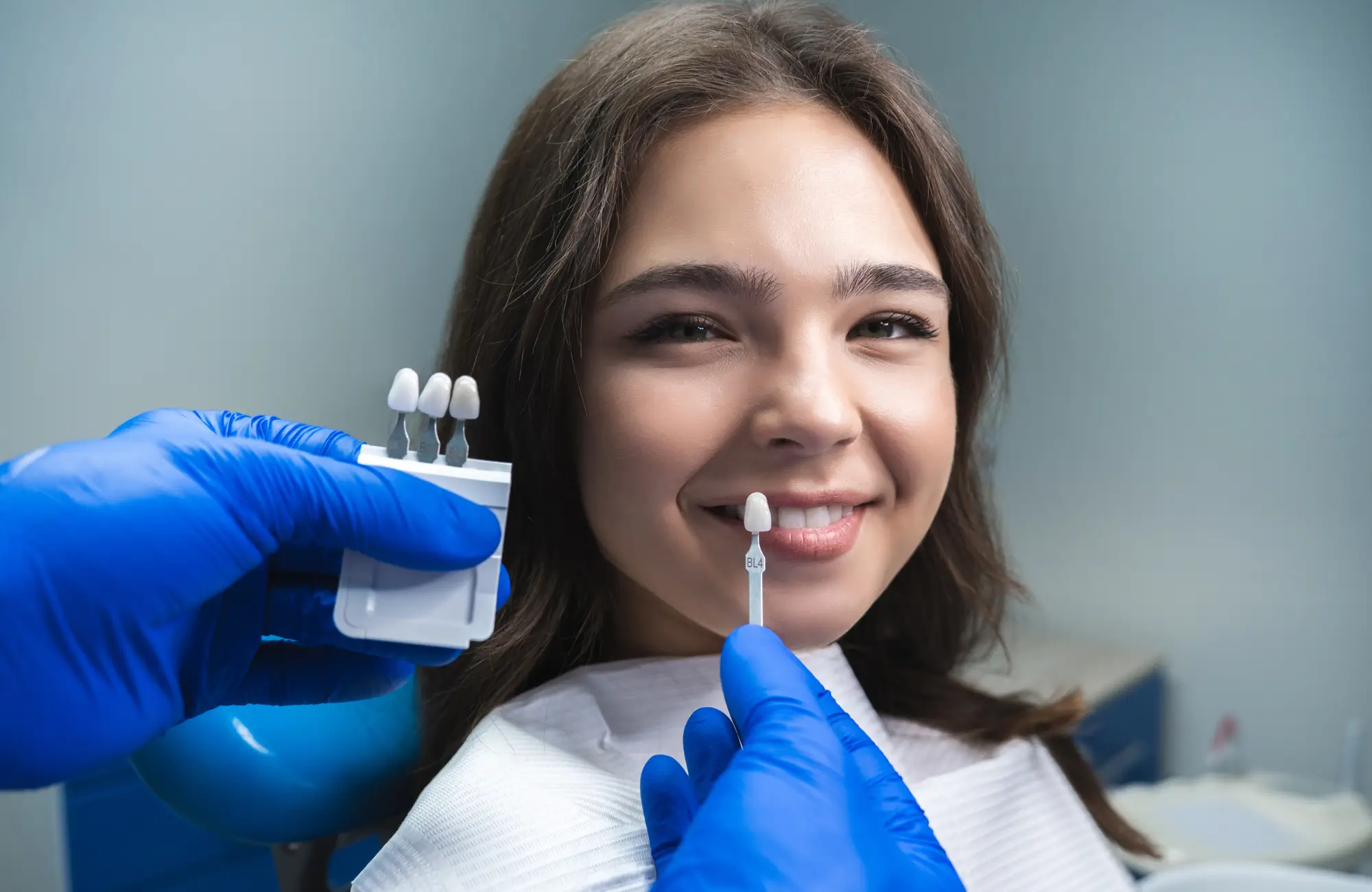 A dentist matches tooth color for a smiling woman's dental treatment.