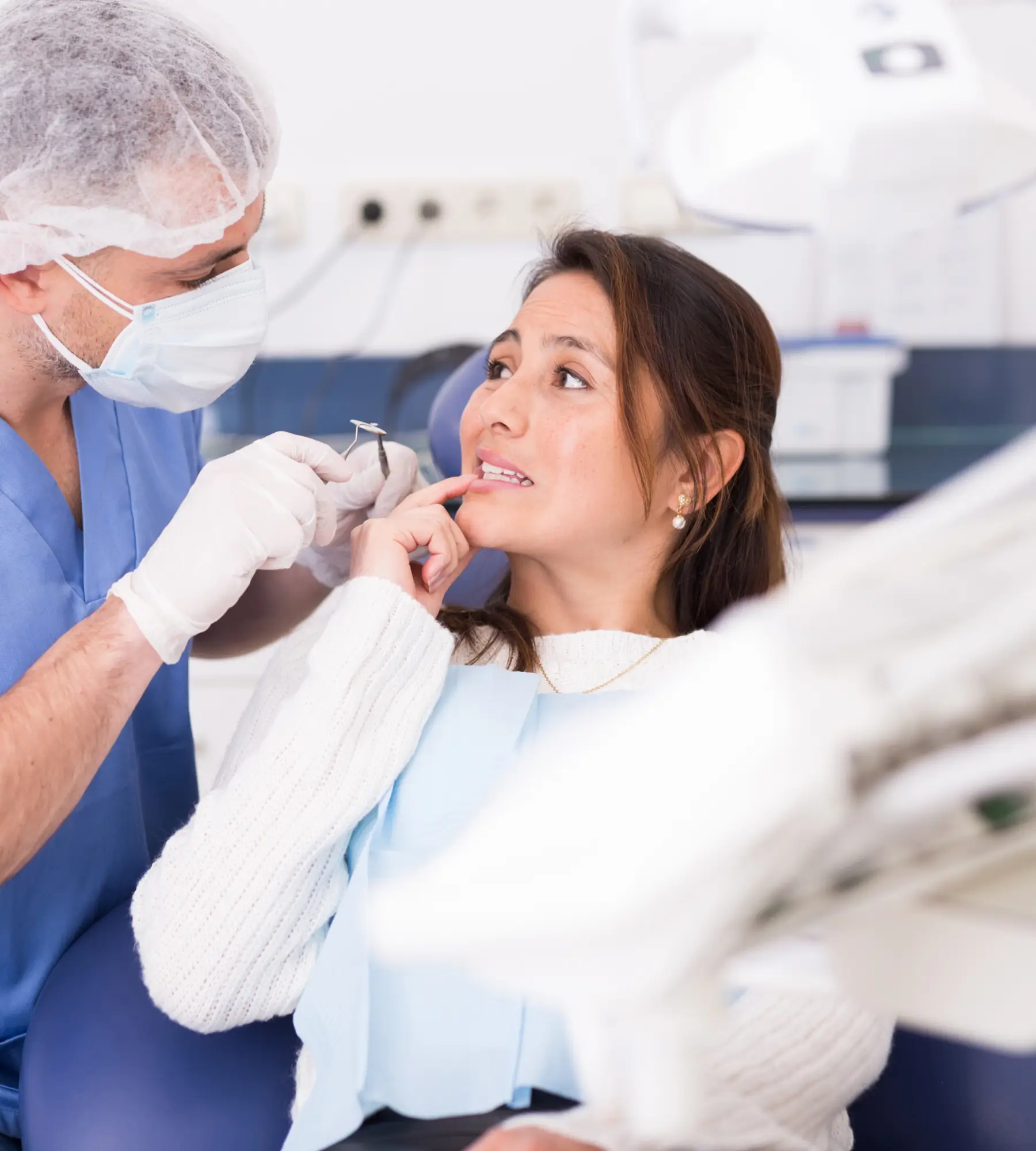 A dentist examines a woman's teeth while she sits in a dental chair.