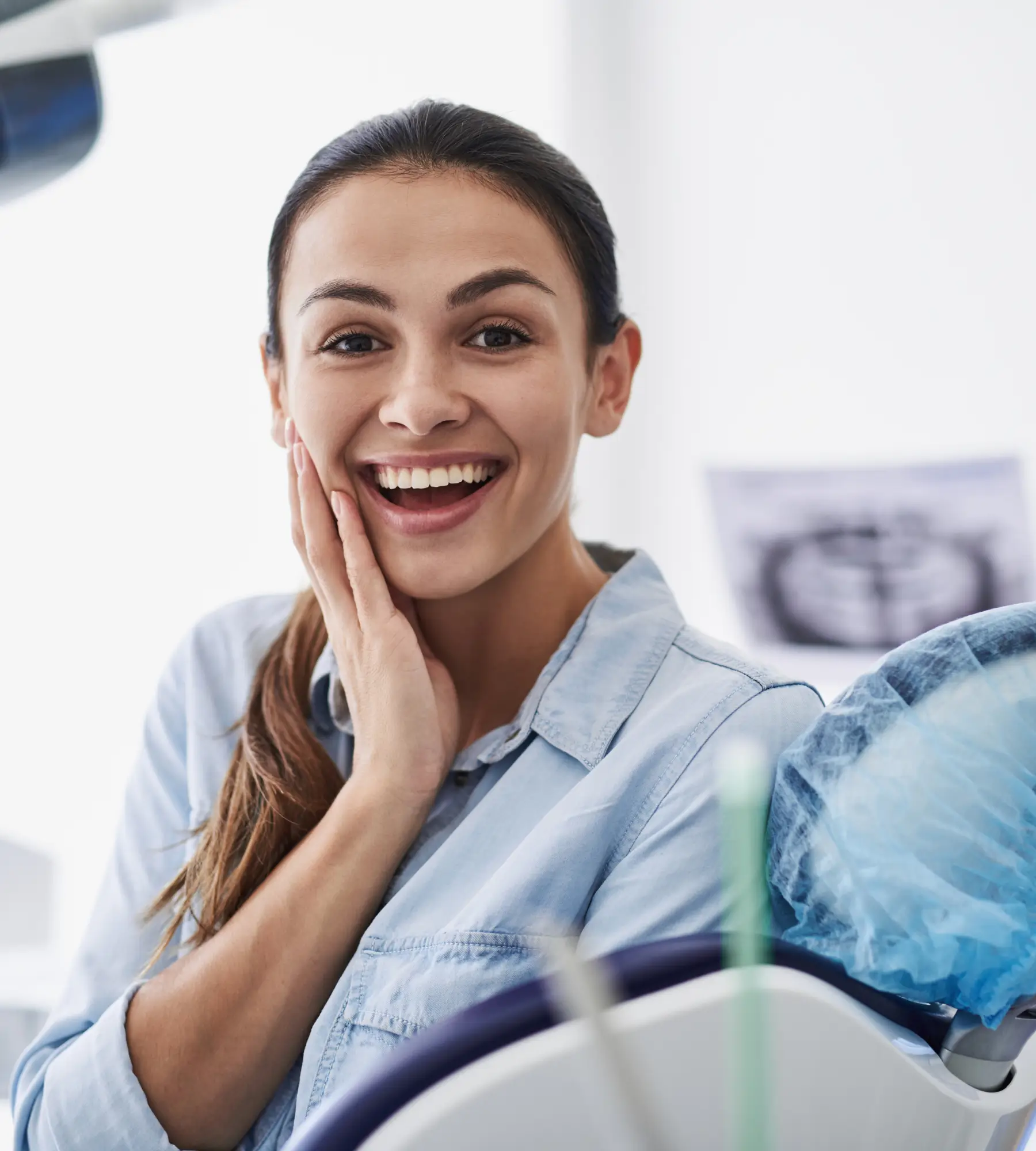 Smiling woman sitting in a dental chair, touching her face with one hand.