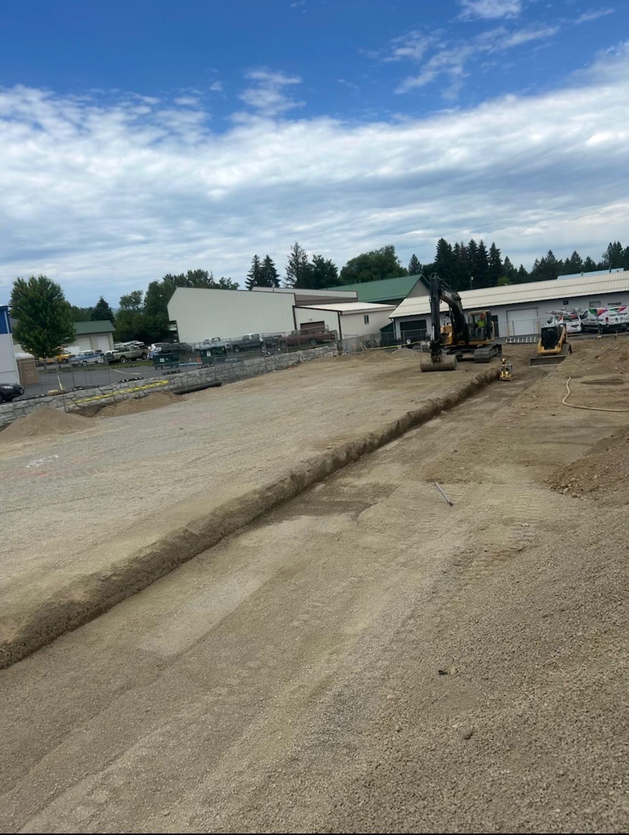 Excavator and a long trench cut across a graded commercial lot in North Idaho