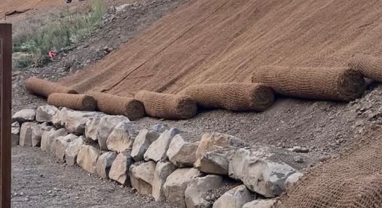 Boulder rock wall at the base of a graded, erosion-blanketed hillside
