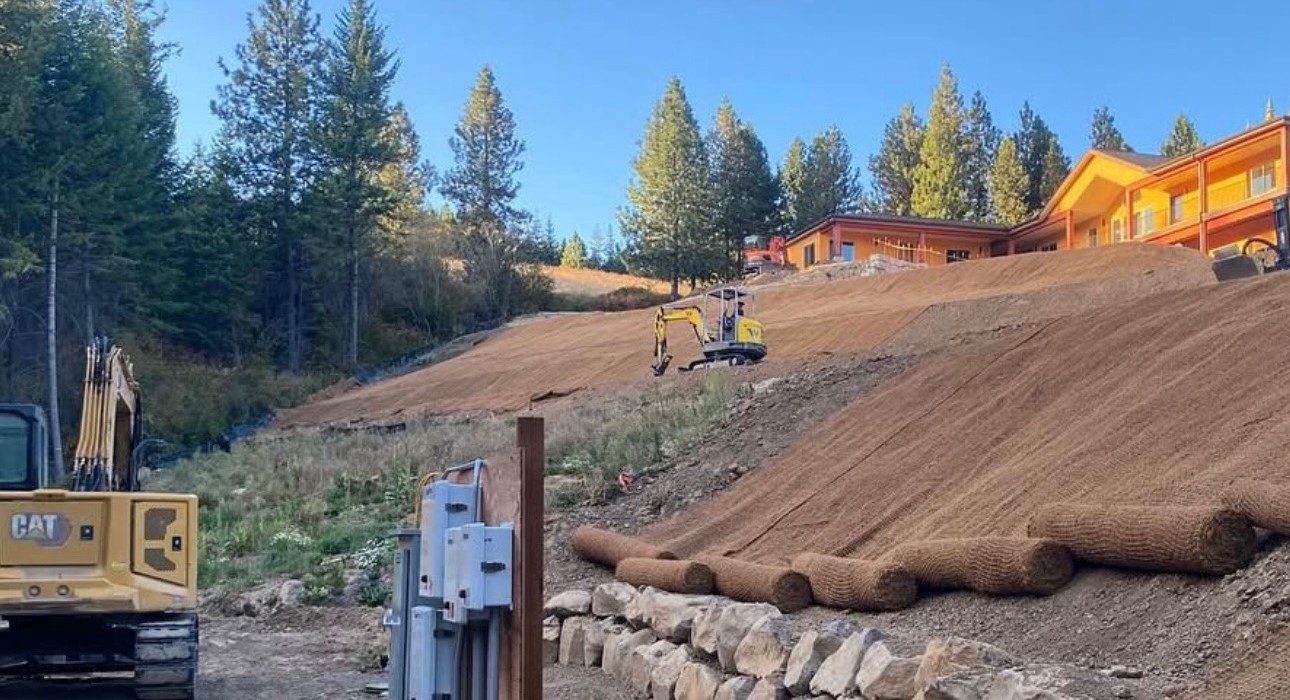 Graded hillside with erosion-control blankets below a wooded home site