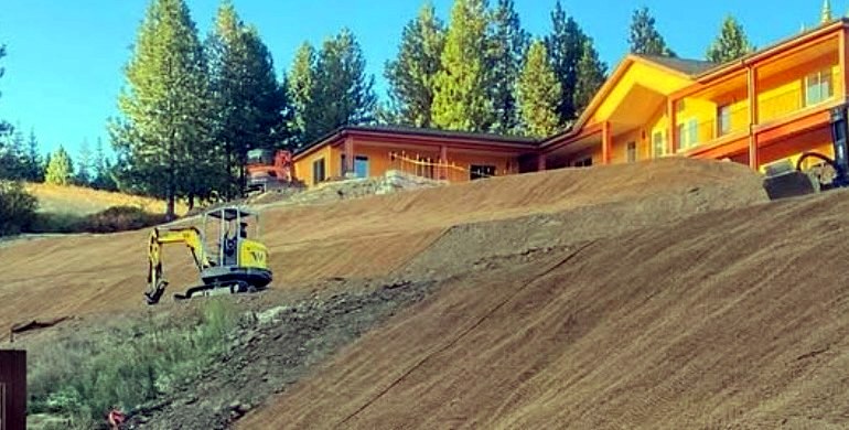 Mini excavator on an erosion-blanketed slope below a new home in North Idaho