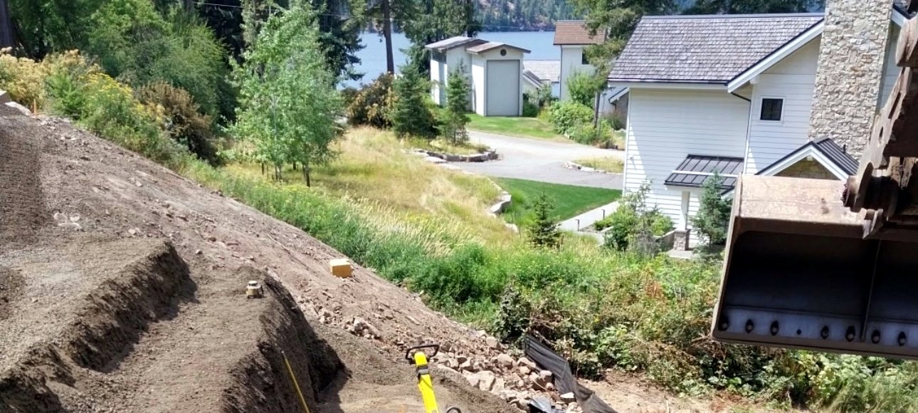 IVR EarthWorks hillside excavation beside a home in North Idaho, with an excavator bucket in frame