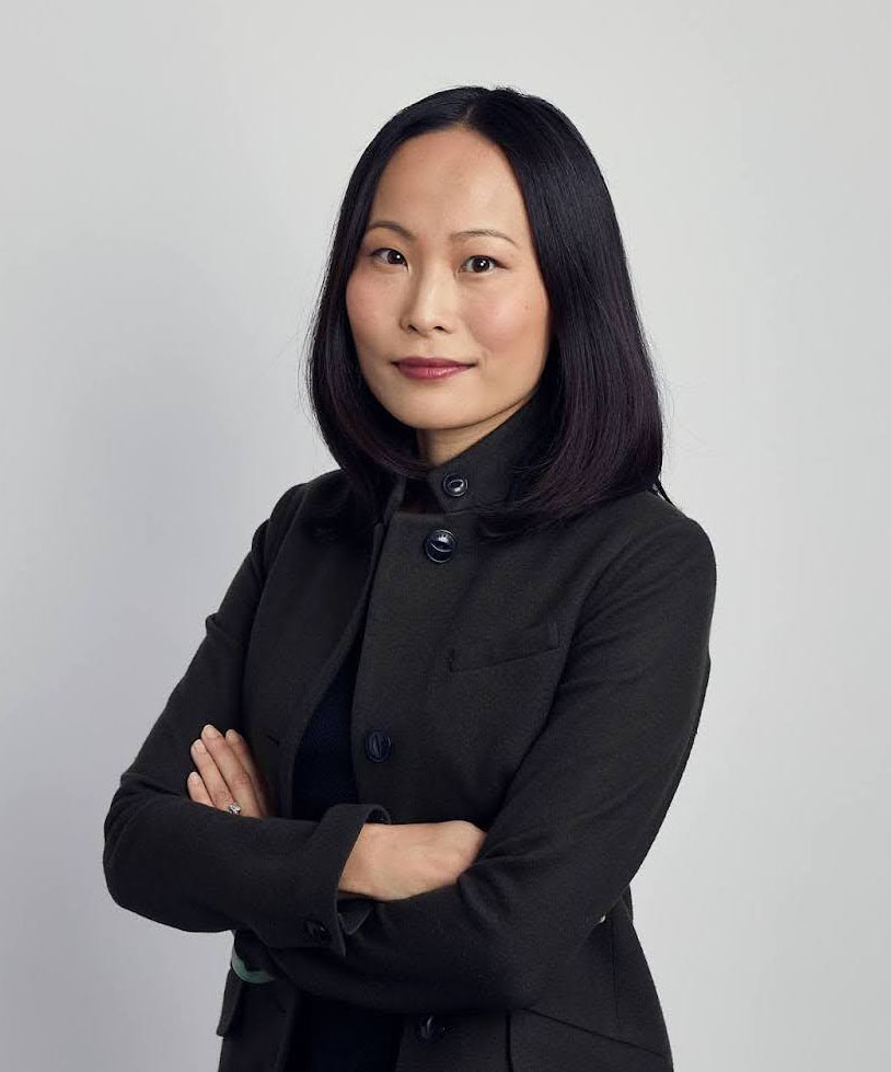 Portrait of Hayley Chan, wearing a black coat, standing with arms crossed.