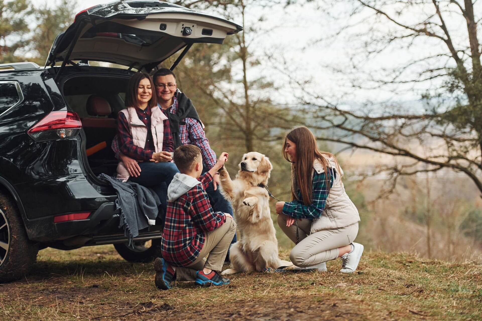 Happy family have fun with their dog near modern car in the outdoors