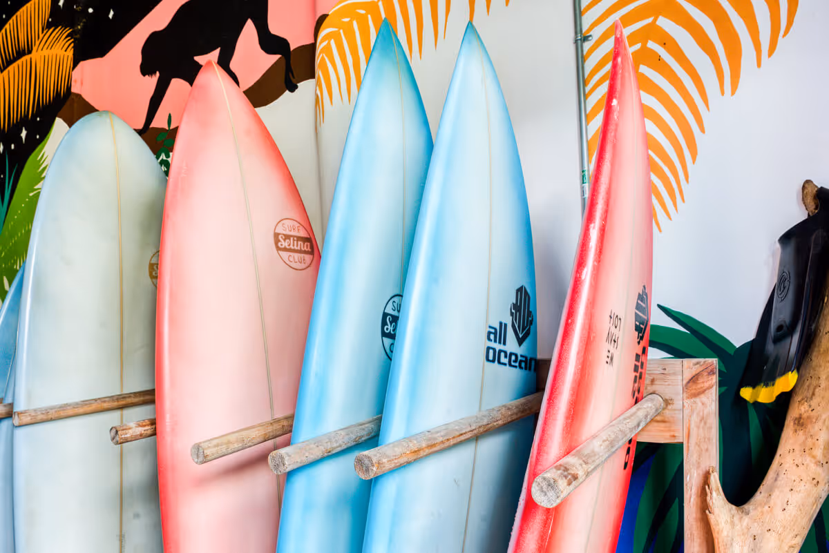 Row of colorful surfboards leaning against a wooden rack with painted tropical mural in the background.