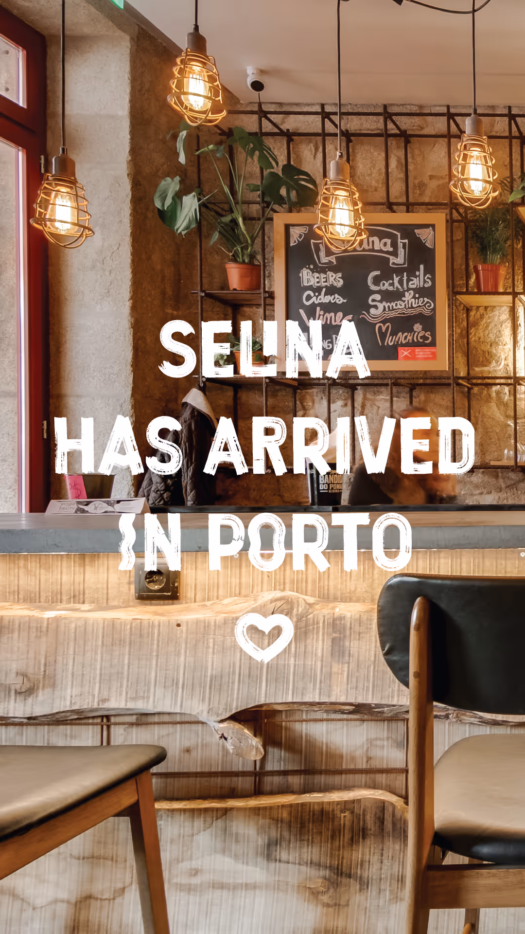 Cozy bar interior with wooden counter, hanging lights, plants, and chalkboard menu in Porto.