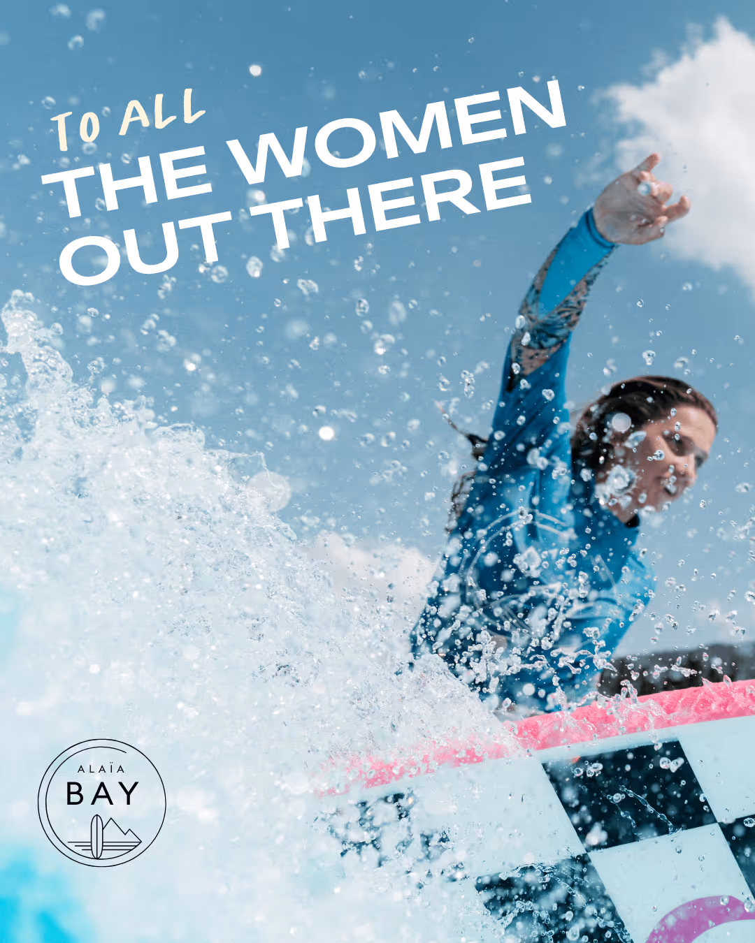 Woman in blue wetsuit surfing with water splashing around her under a blue sky.
