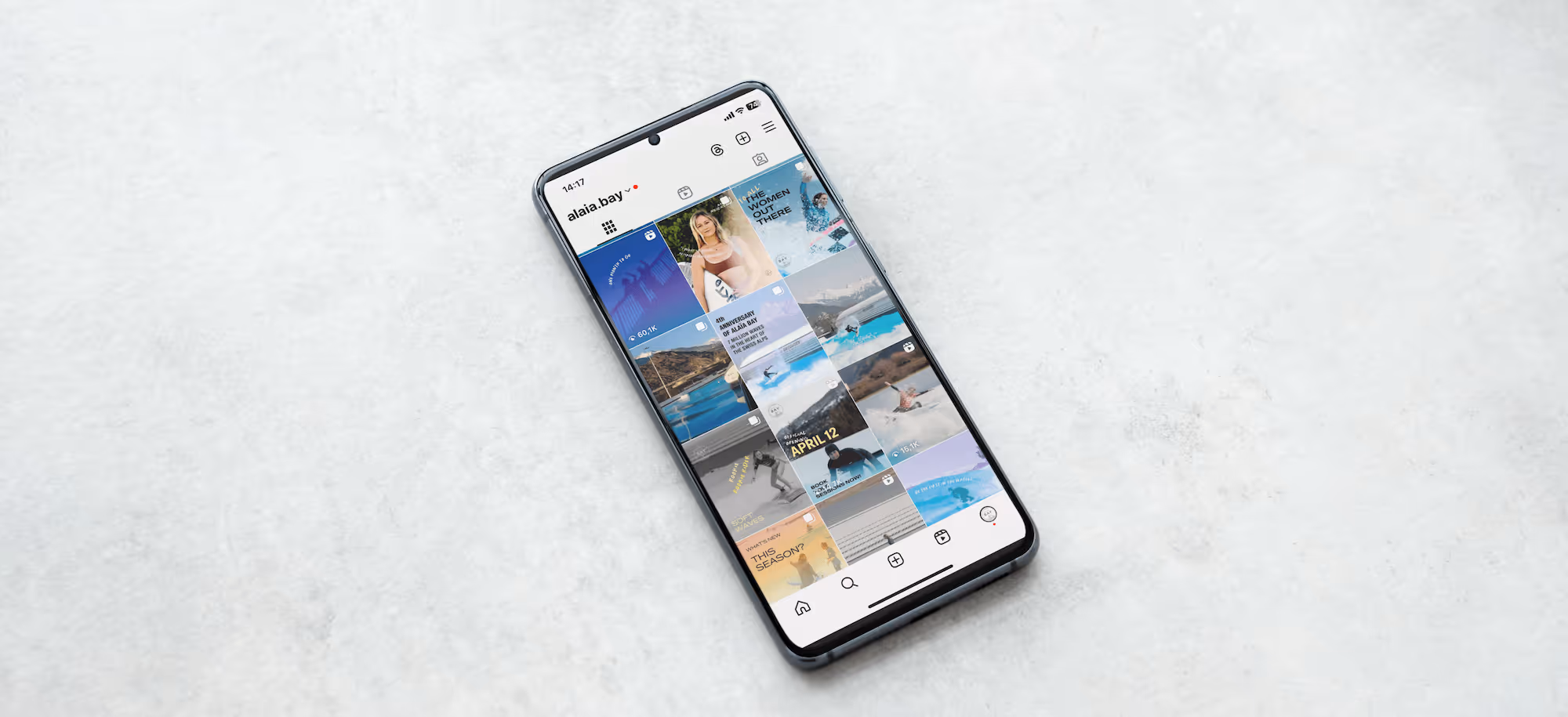 Smartphone on a light surface showing an Instagram profile with photos and videos in a grid layout.
