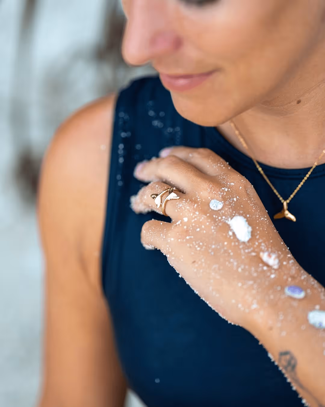 Close-up of a woman wearing a whale tail ring and necklace with sand on her hand and arm.
