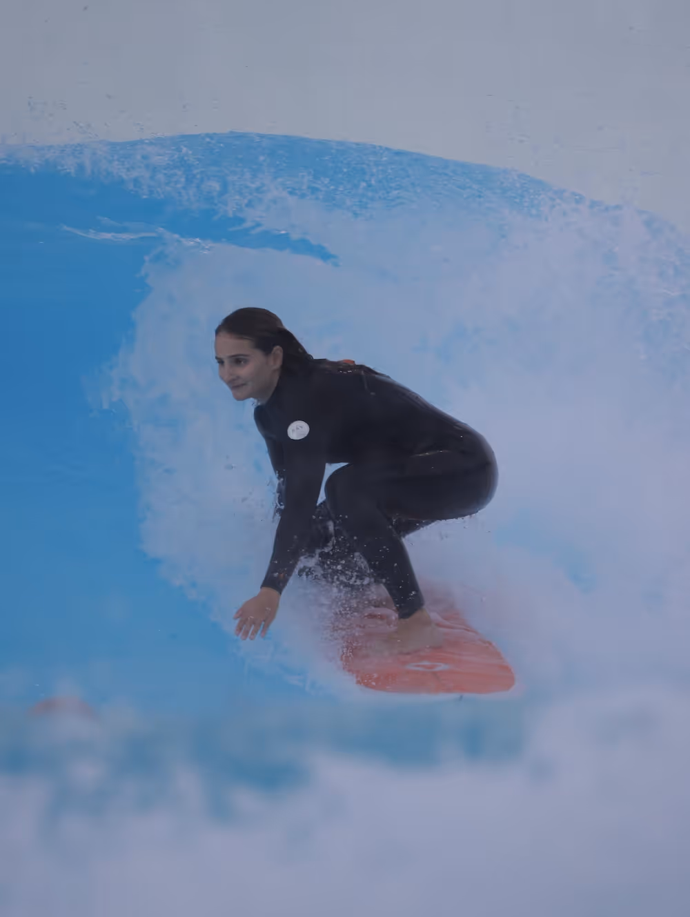 Woman in black wetsuit surfing on an orange board inside a curling blue wave.