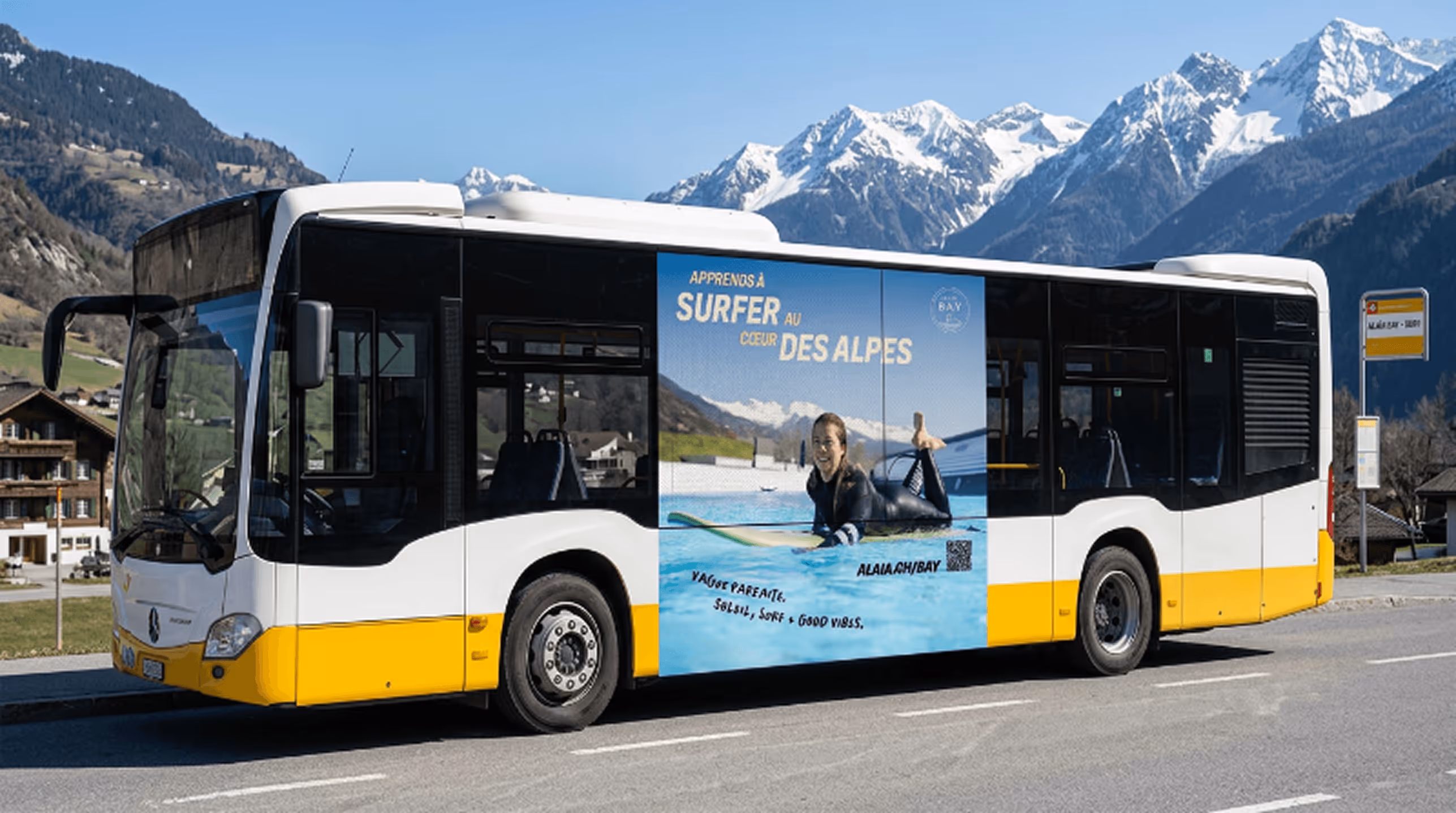 Yellow and white bus with an advertisement showing a woman surfing, mountains in background.